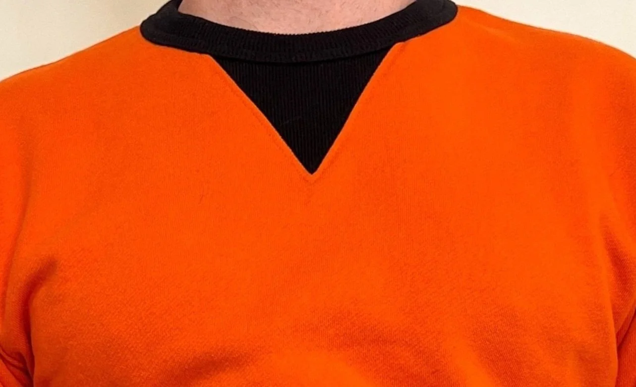 Close-up of a person wearing an orange garment with a black collar, showing the upper chest and neck area.