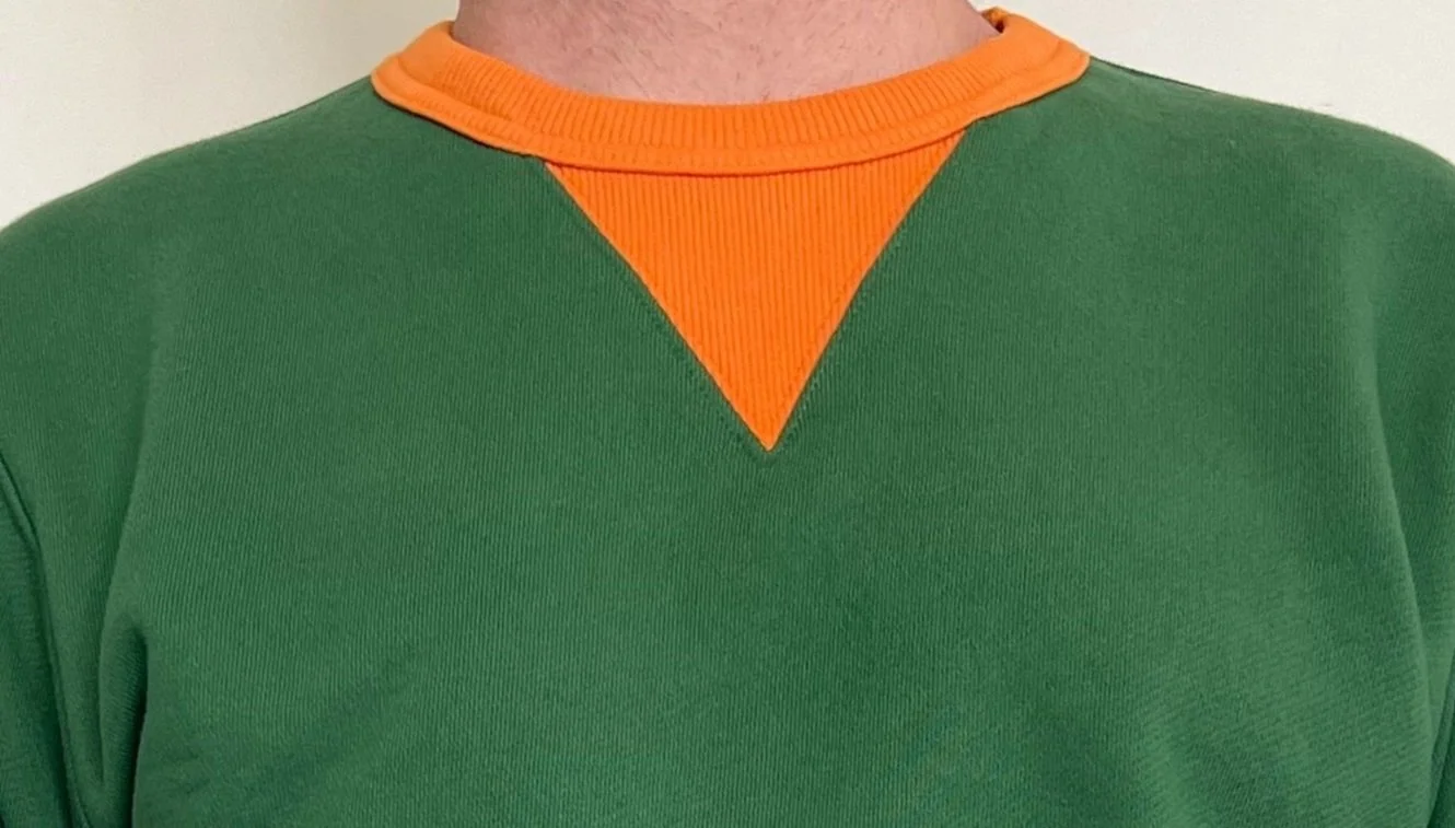 A person wearing a green sweatshirt with an orange collar and a sewn-in orange triangle detail at the neckline.