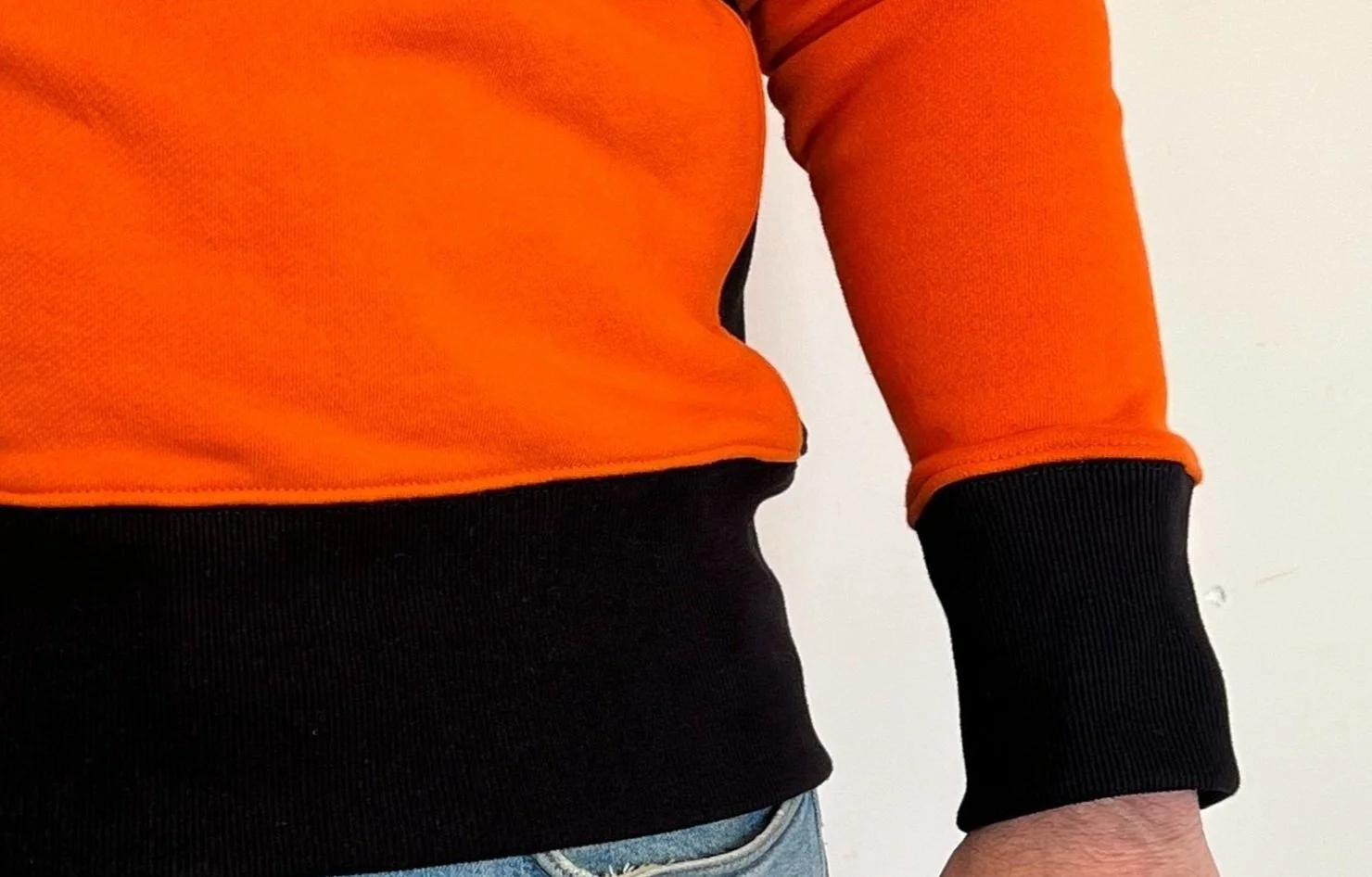 Close-up of a person wearing an orange and black sweatshirt with denim jeans.