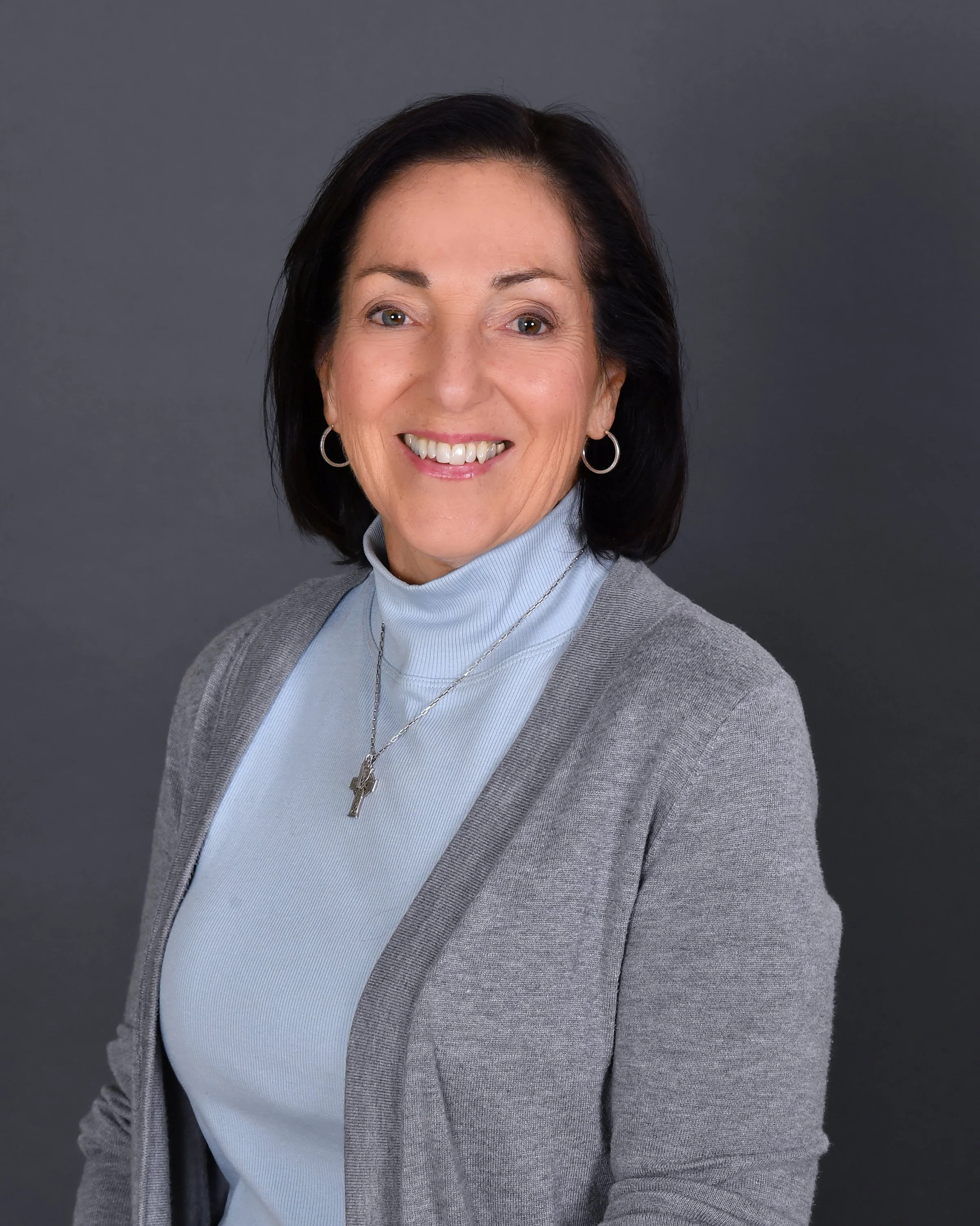 A woman smiling outdoors near a waterfall and lush greenery.