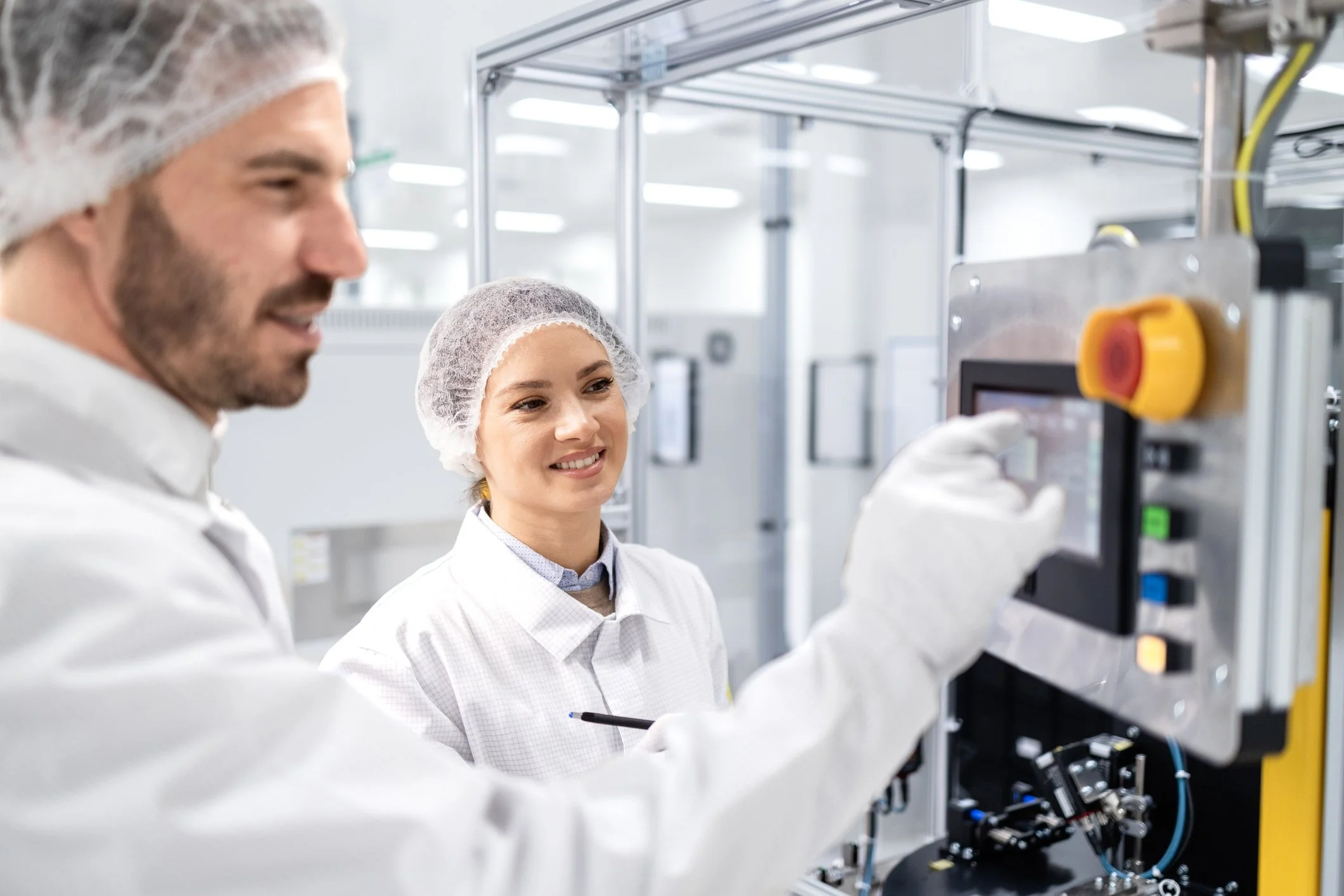 Cleanroom technicians in hairnets and protective clothing operate industrial manufacturing equipment.