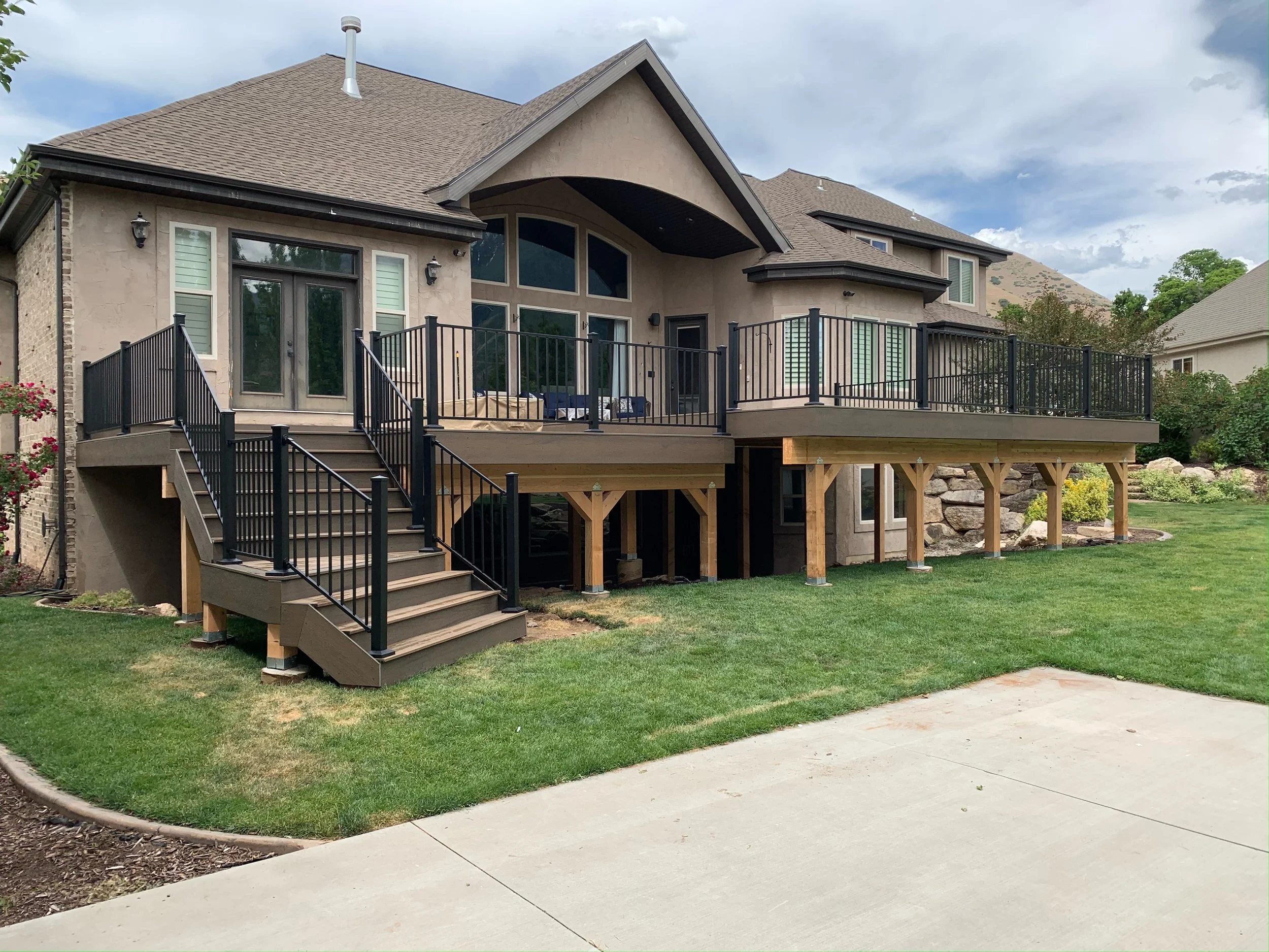 Newly built wooden deck with black metal railing attached to the back of a house, with stairs leading down to a grassy yard.