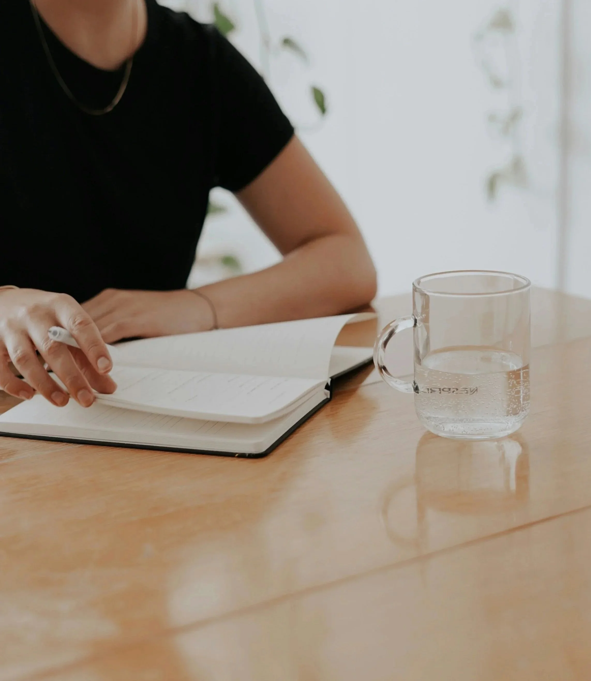 Person writing in a notebook beside a glass of water, representing preparation for a therapy session.