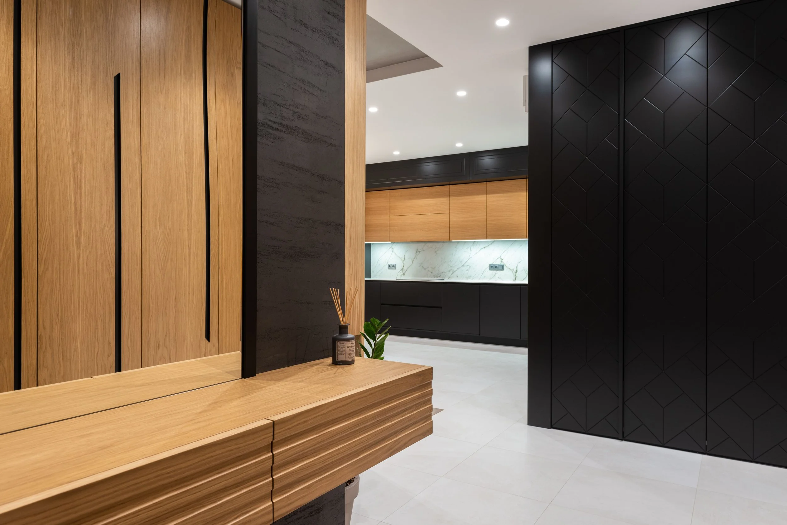Modern interior space with wooden slat wall, a black patterned cabinet, marble backsplash, and recessed lighting.