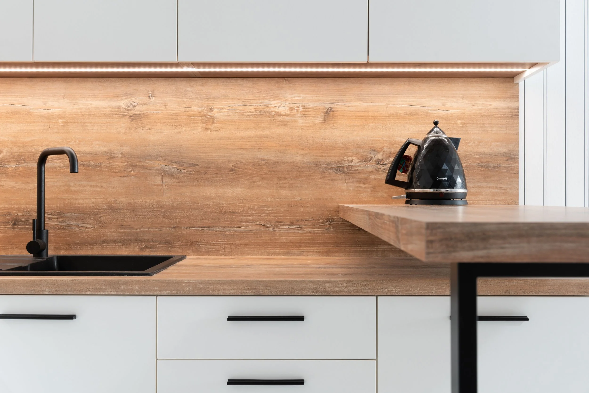 Modern kitchen with white cabinets, wood countertop, black sink faucet, and a black electric kettle on the counter.