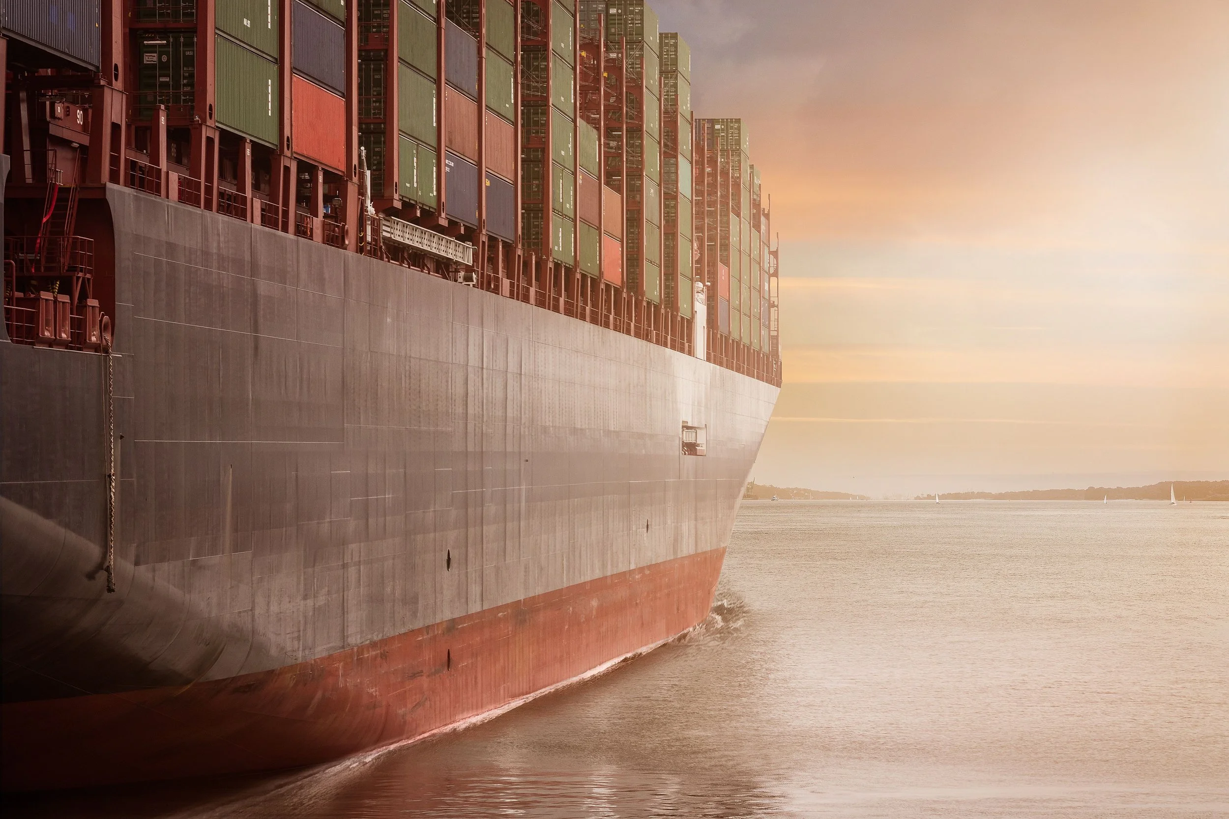 A large cargo ship with colorful containers on its deck sailing in a body of water at sunset.