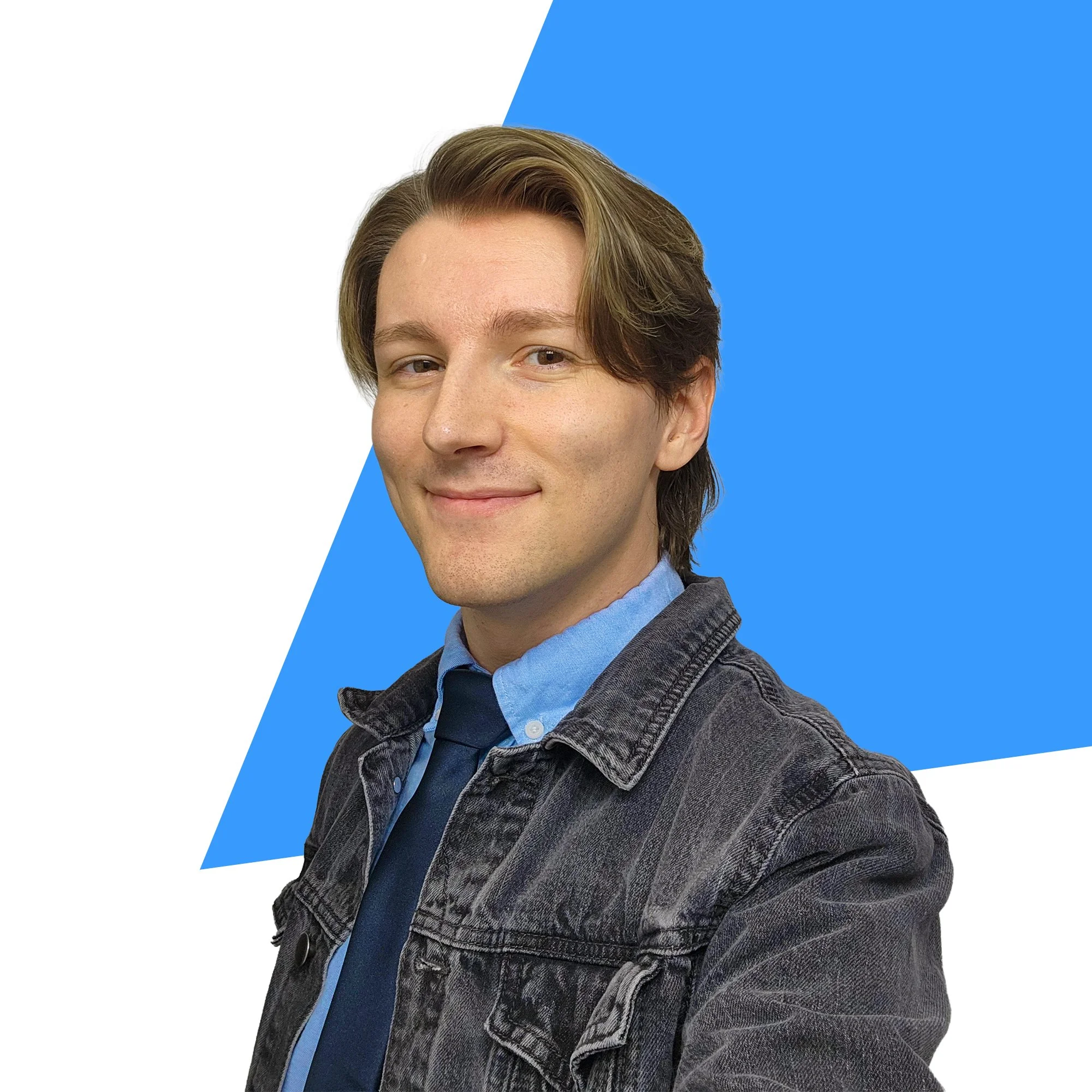 Close-up portrait of young man with light skin, brown hair, wearing a denim jacket and blue shirt, smiling, with a background of a white and blue geometric pattern.
