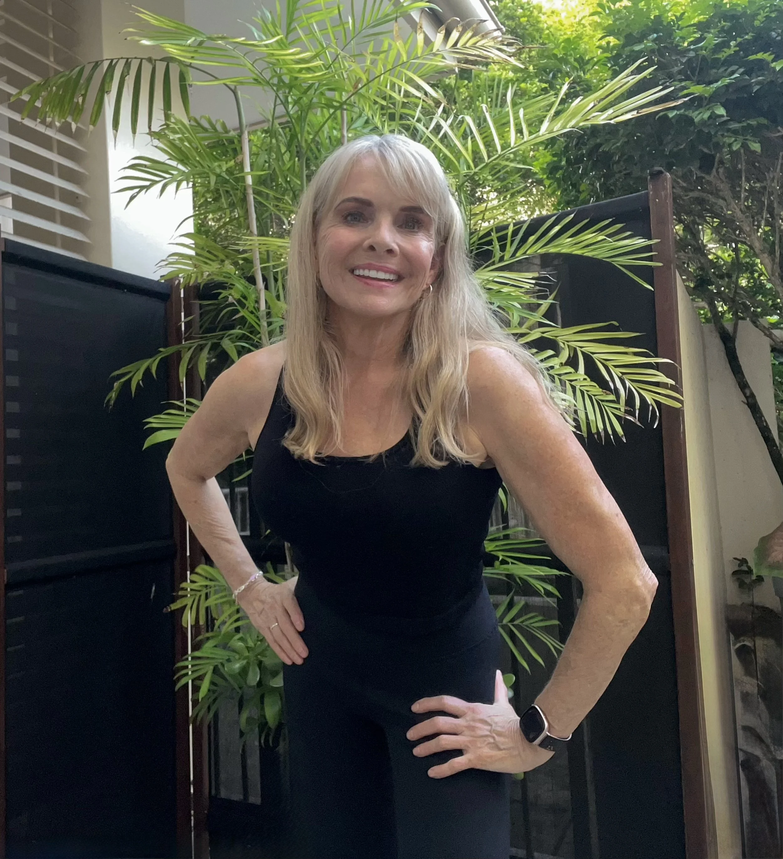 Image of a personal trainer smiling with arms on her hips and green trees in the background