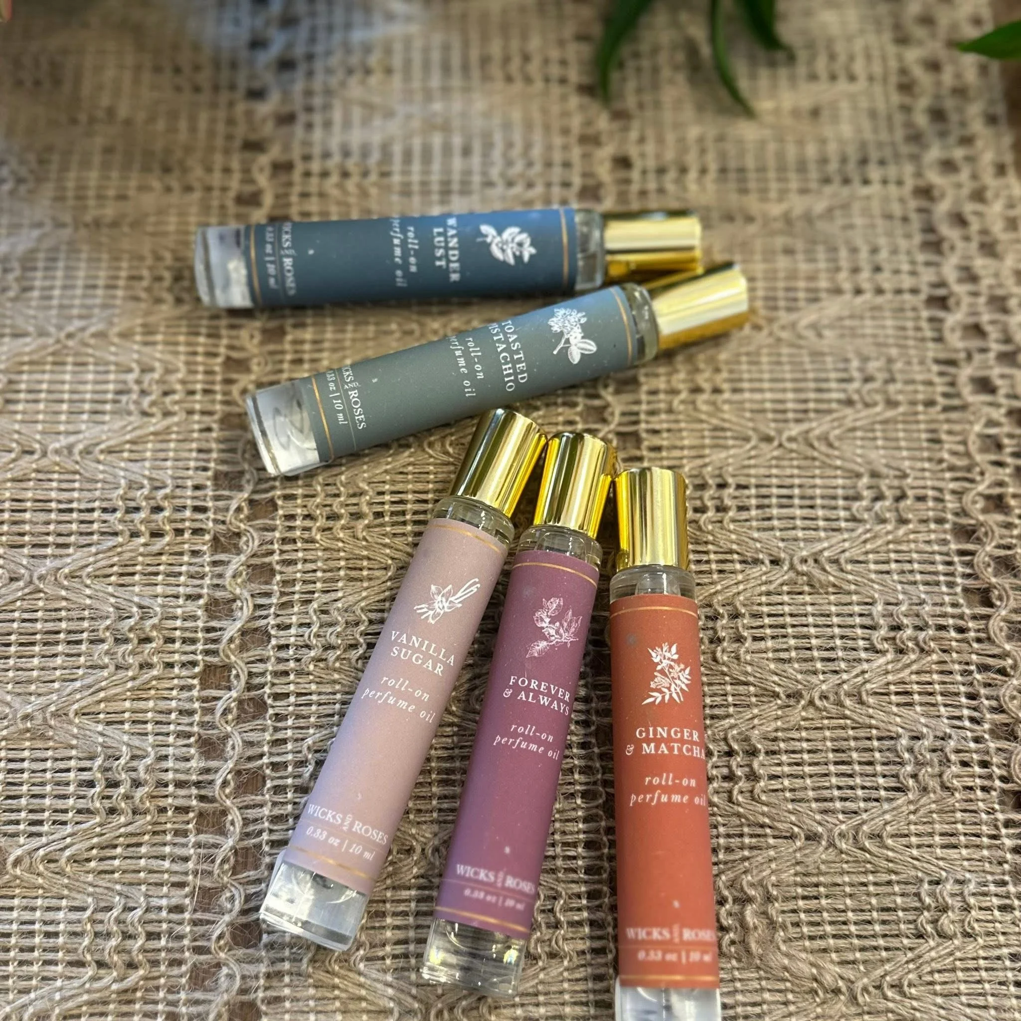 Several roll-on perfume bottles with gold caps, labeled Vanilla Sugar, Forever & Always, and Ginger & Matcha, placed on a textured woven surface.