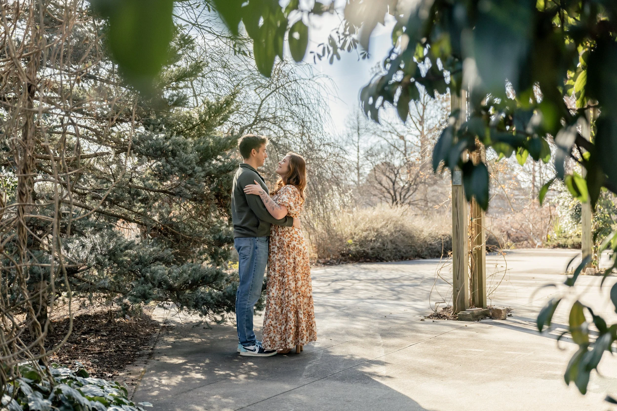 Natural, candid moment of couple sitting closely on a wooden garden bench surrounded by greenery at JC Raulston Arboretum.