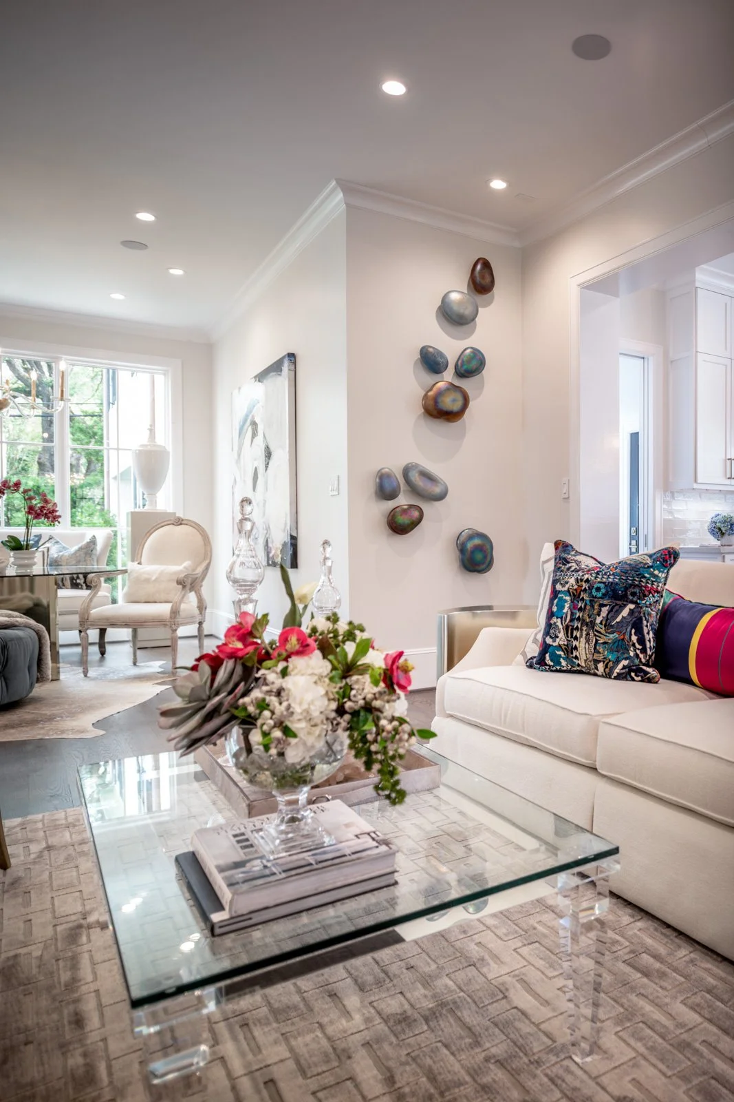 Luxury River Oaks living room designed by The Design Firm in Houston, featuring a white upholstered sofa, colorful accent pillows, glass coffee table, floral arrangement, and contemporary wall sculptures.