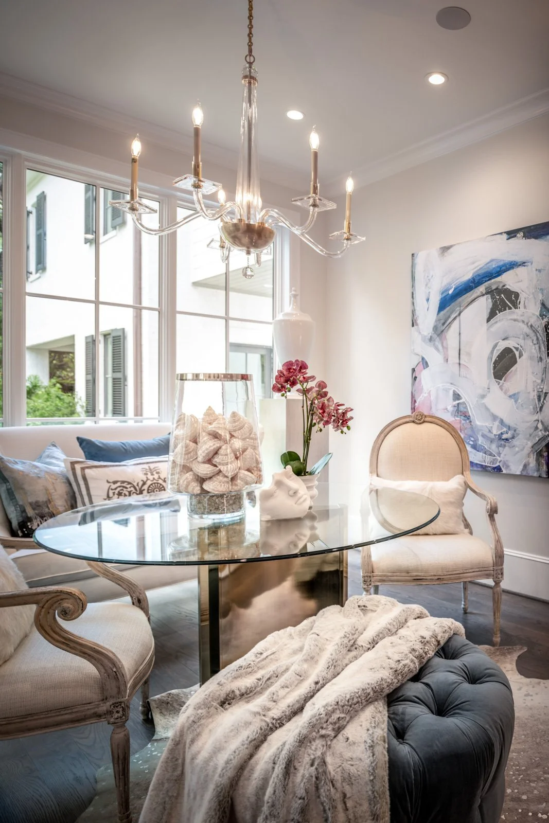 Elegant River Oaks dining room by The Design Firm in Houston, featuring a round glass dining table, upholstered dining chairs, decorative chandelier, contemporary artwork, and custom furnishings.