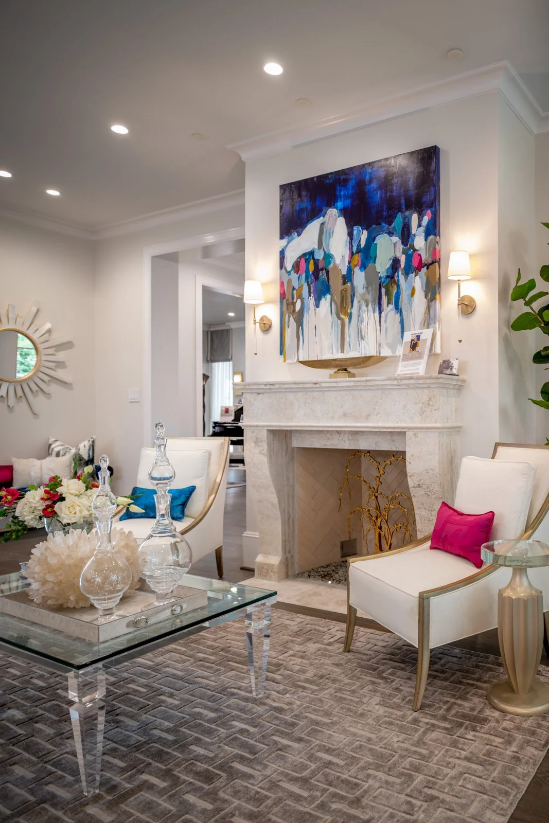 Elegant River Oaks living room featuring a custom stone fireplace, colorful contemporary artwork, upholstered accent chairs, and sophisticated furnishings by The Design Firm in Houston.
