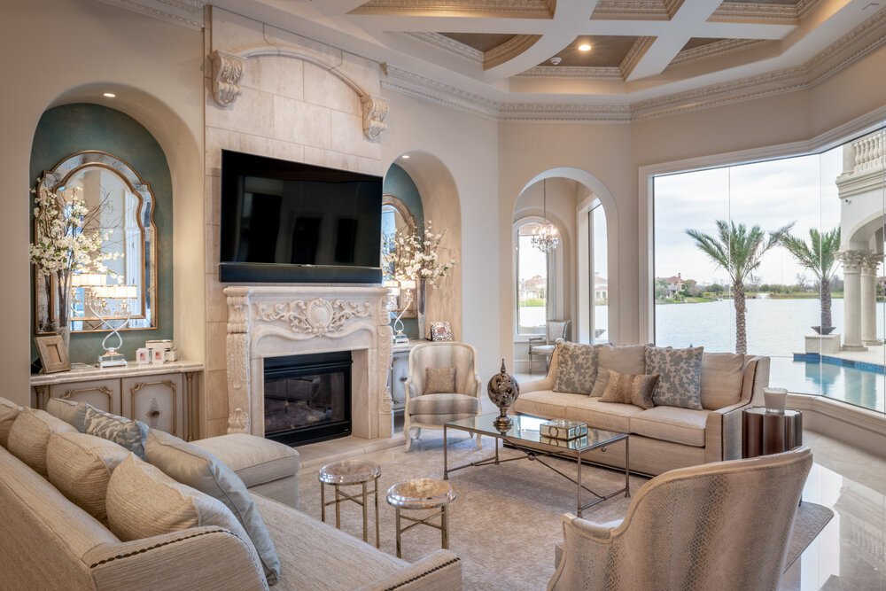 Traditional luxury living room in Sugar Land, Texas, featuring an ornate fireplace, elegant neutral furnishings, decorative ceiling details, and lake views.