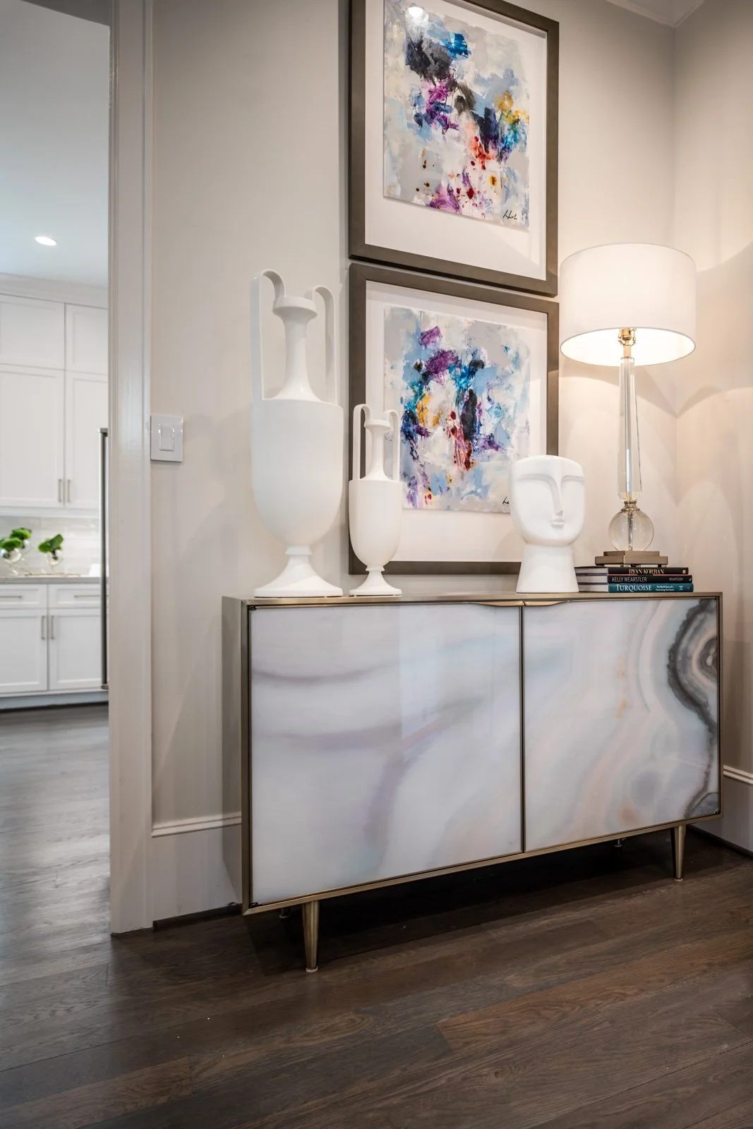 Elegant River Oaks home interior featuring a contemporary console cabinet, colorful abstract artwork, sculptural white accessories, and decorative lighting selected by The Design Firm in Houston. Copy