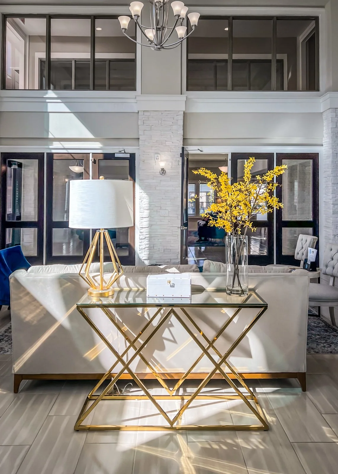 Commercial decorator seating area with a cream sofa and a glass and gold console table with a lamp.