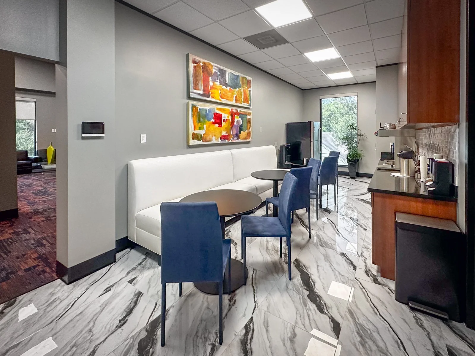 Employee lounge designed by The Design Firm for a large vision care business, featuring contemporary blue seating, round tables, a white upholstered banquette, and a welcoming space for employees to relax. 