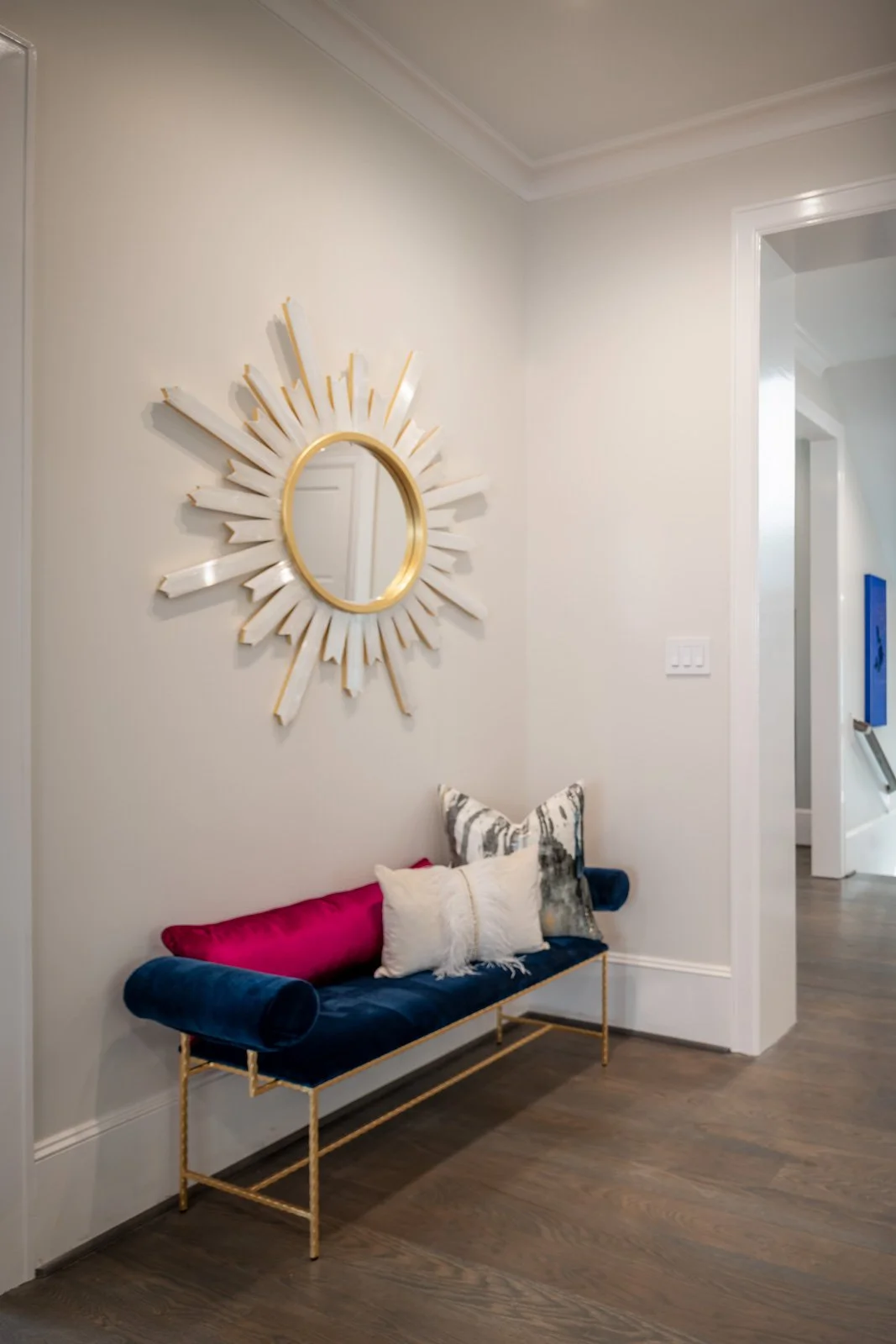 Elegant River Oaks entryway designed by The Design Firm in Houston, featuring a gold sunburst mirror, navy blue velvet bench, colorful accent pillows, and sophisticated decorative details. Copy
