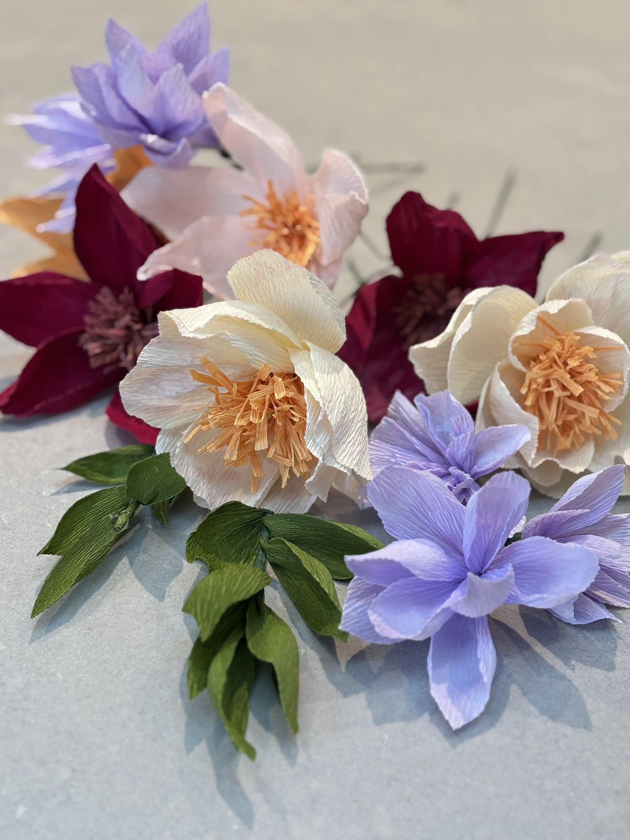 Artificial flowers in purple, cream, red, and peach colors with green leaves on a light background.