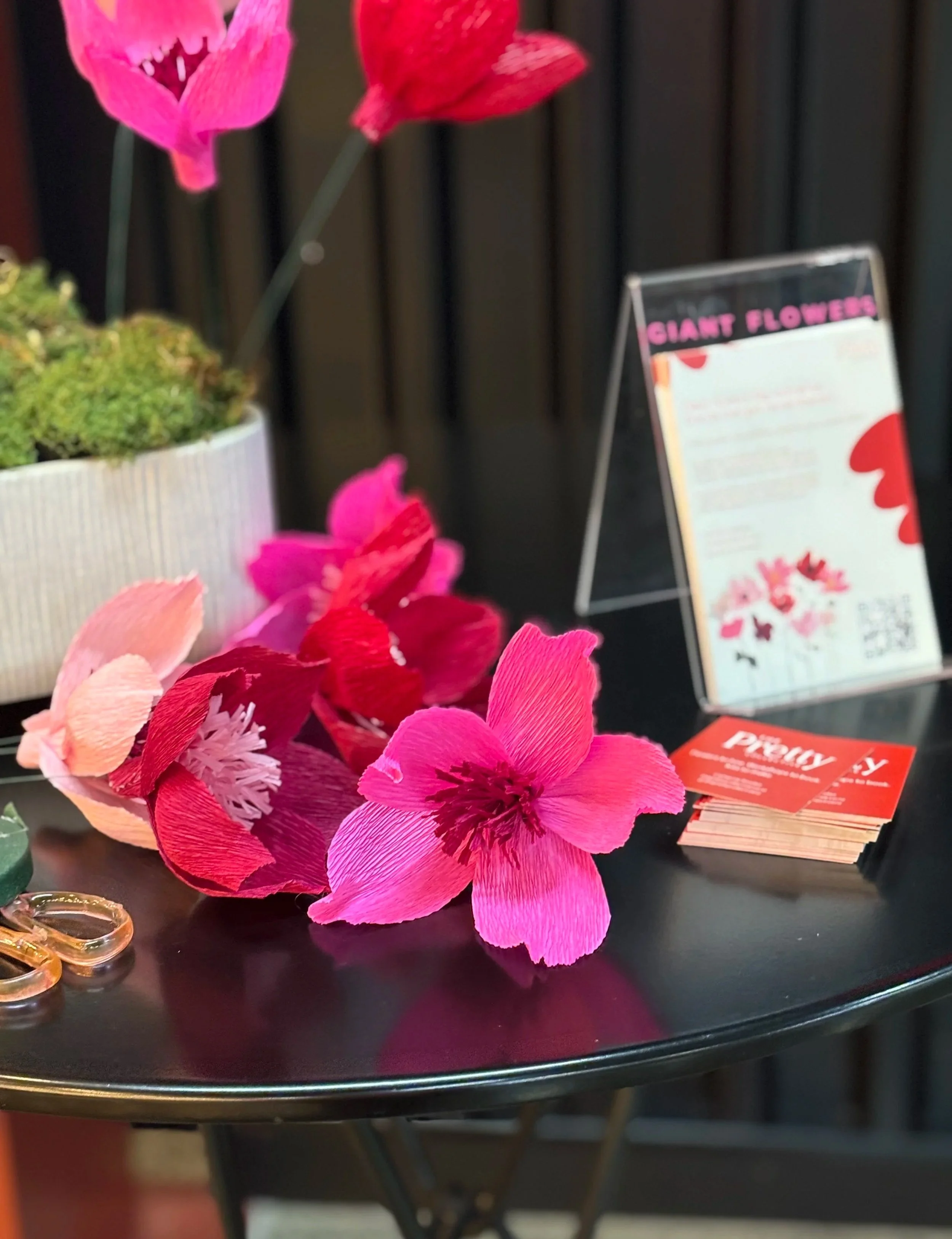 Close-up of pink and red artificial flowers displayed on a black surface, with signs and other items in the background.