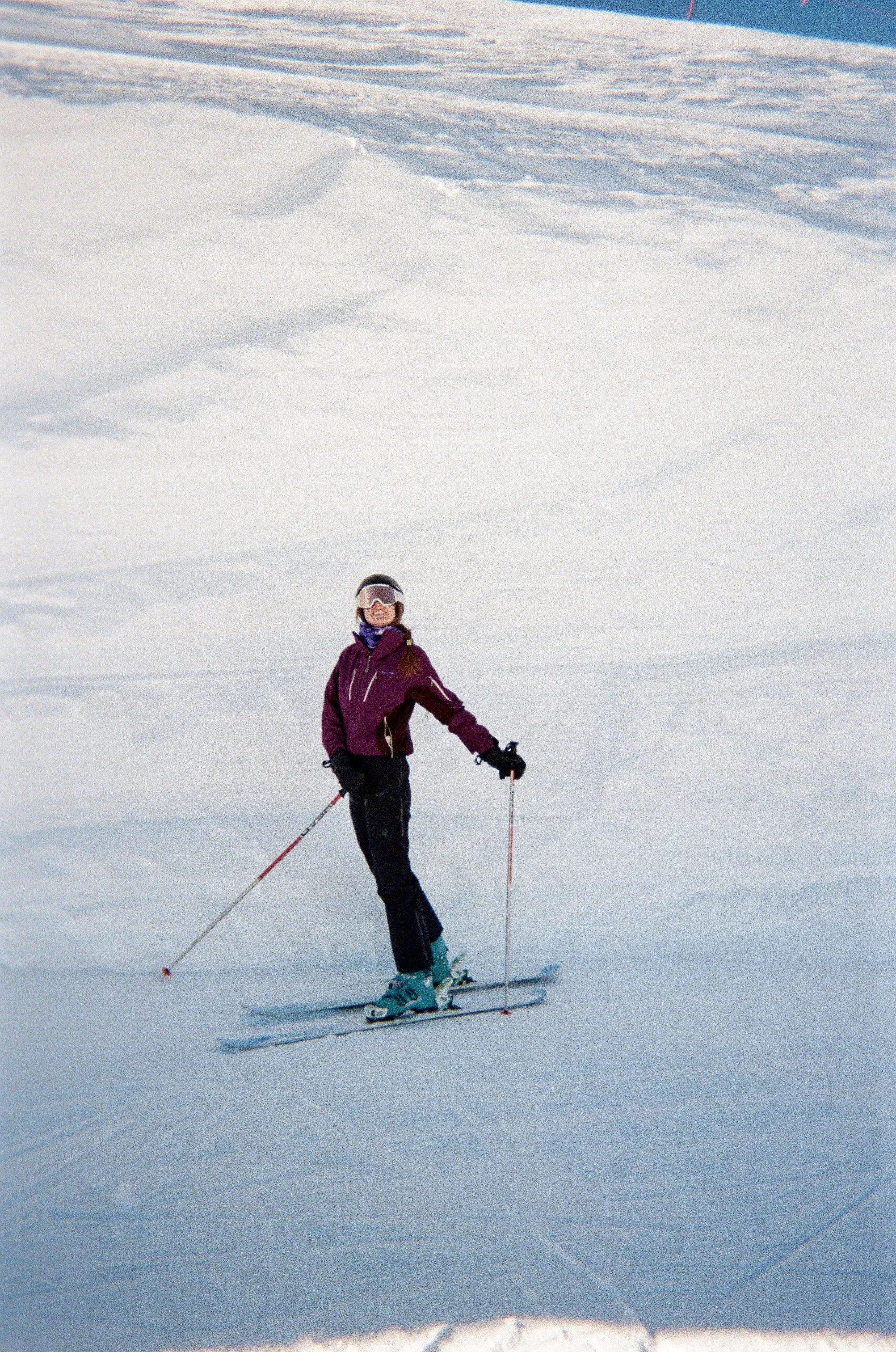 A woman skiing on a snow-covered slope, wearing a purple jacket, black snow pants, a helmet, and goggles.