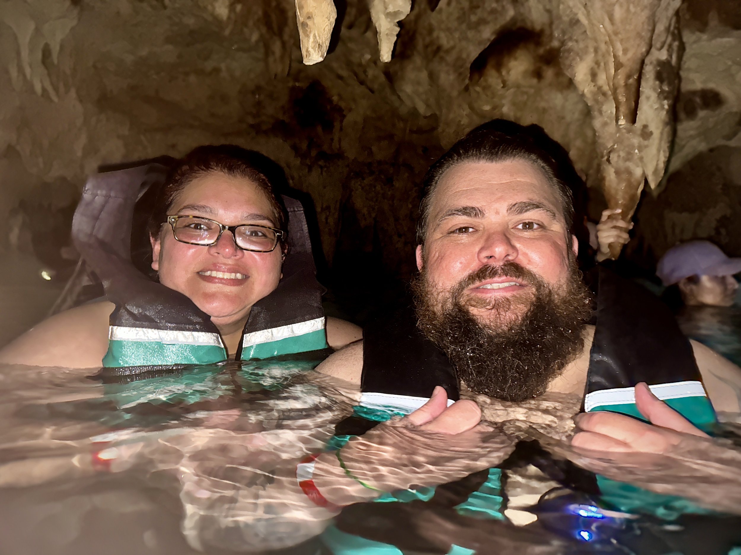 Two people smiling while wearing life jackets in a cave pool.