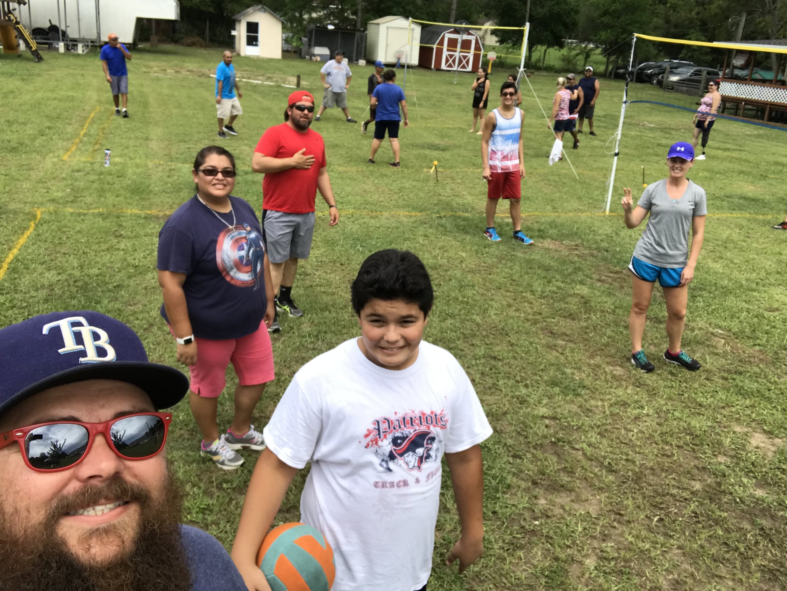 Group of people playing volleyball outdoors, smiling, with a person holding a volleyball in the foreground.