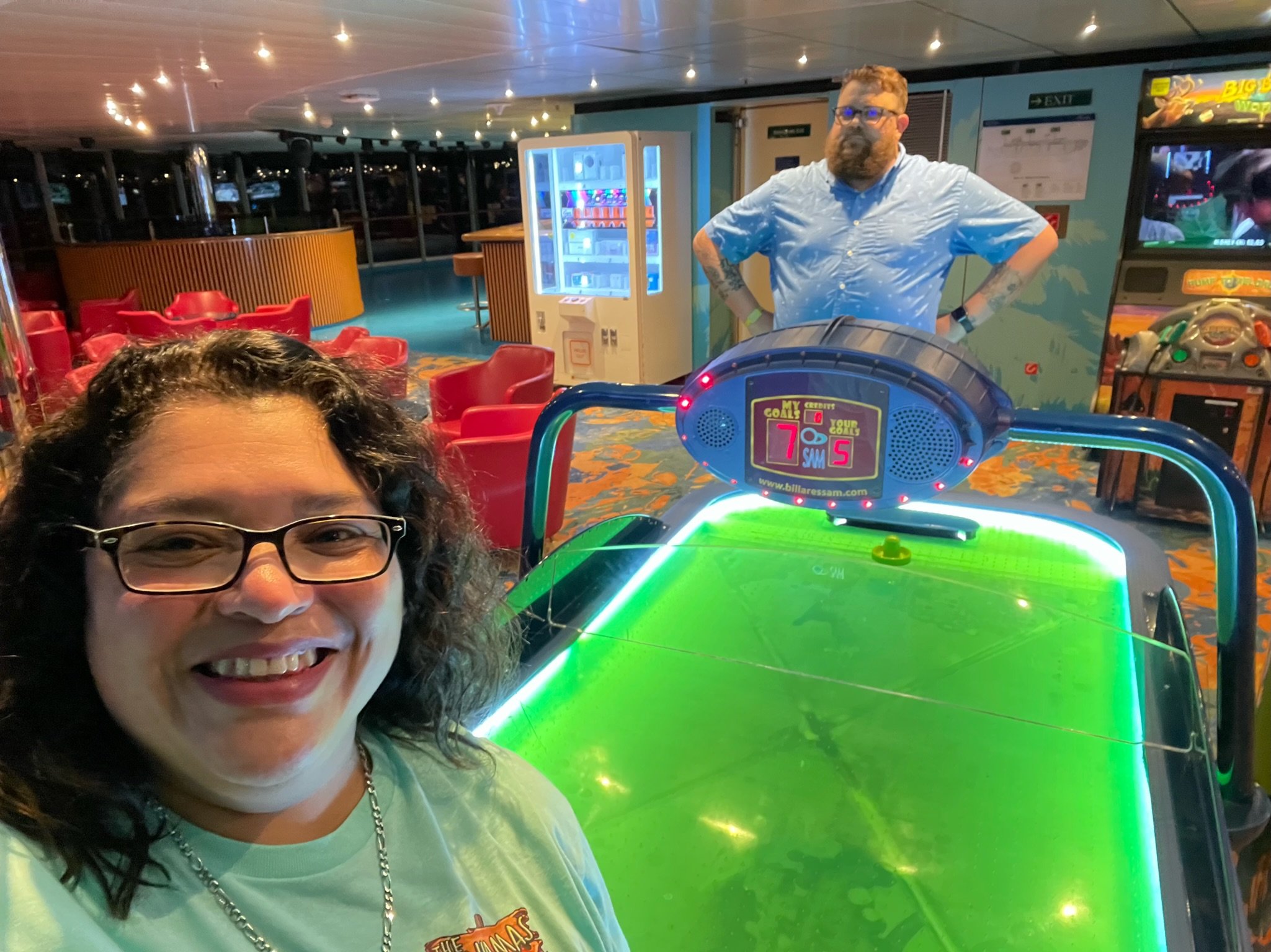 Two people in an arcade with an air hockey table and vending machine in the background.
