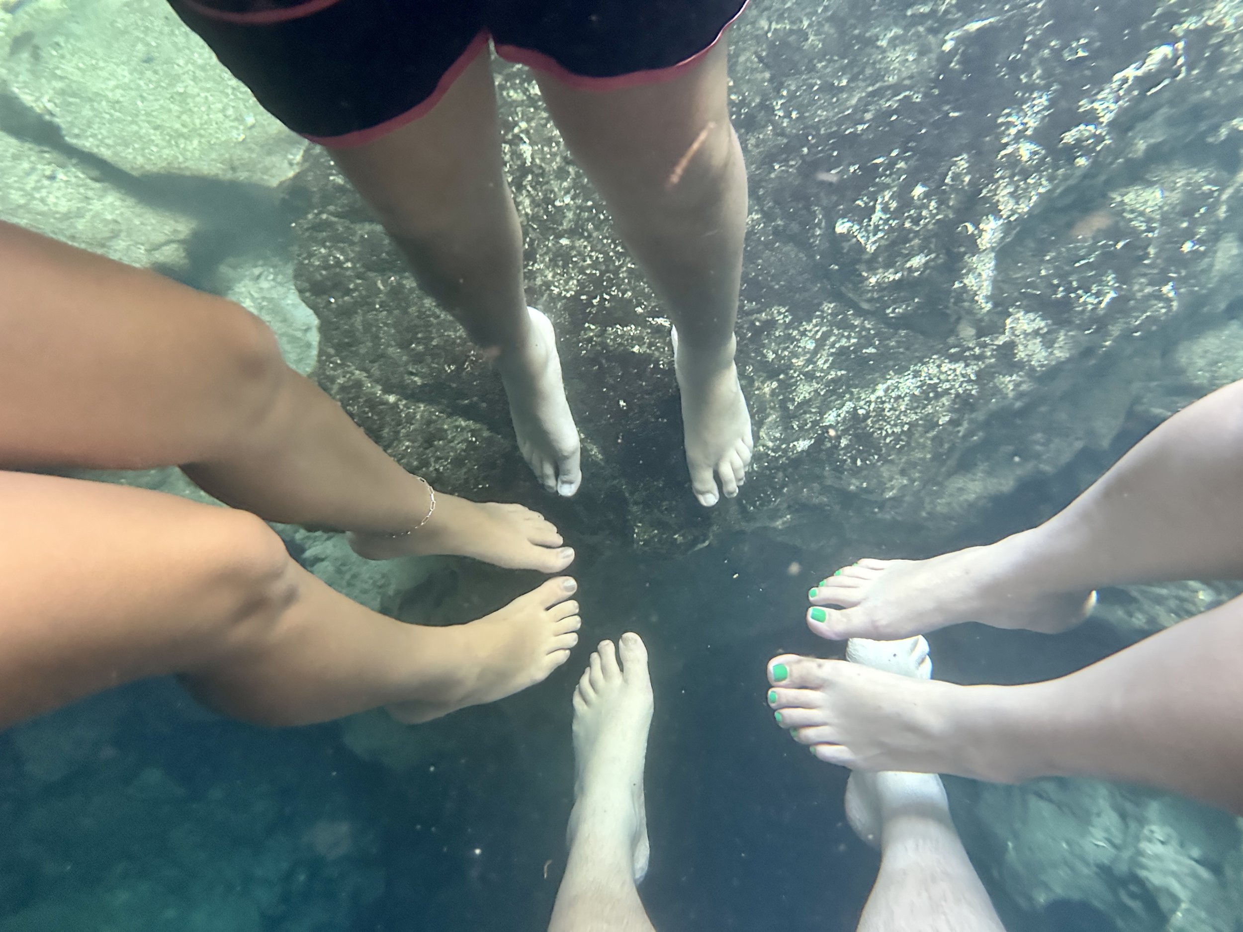 Underwater photo of three people with bare feet in a natural water setting, with rock and water visible.