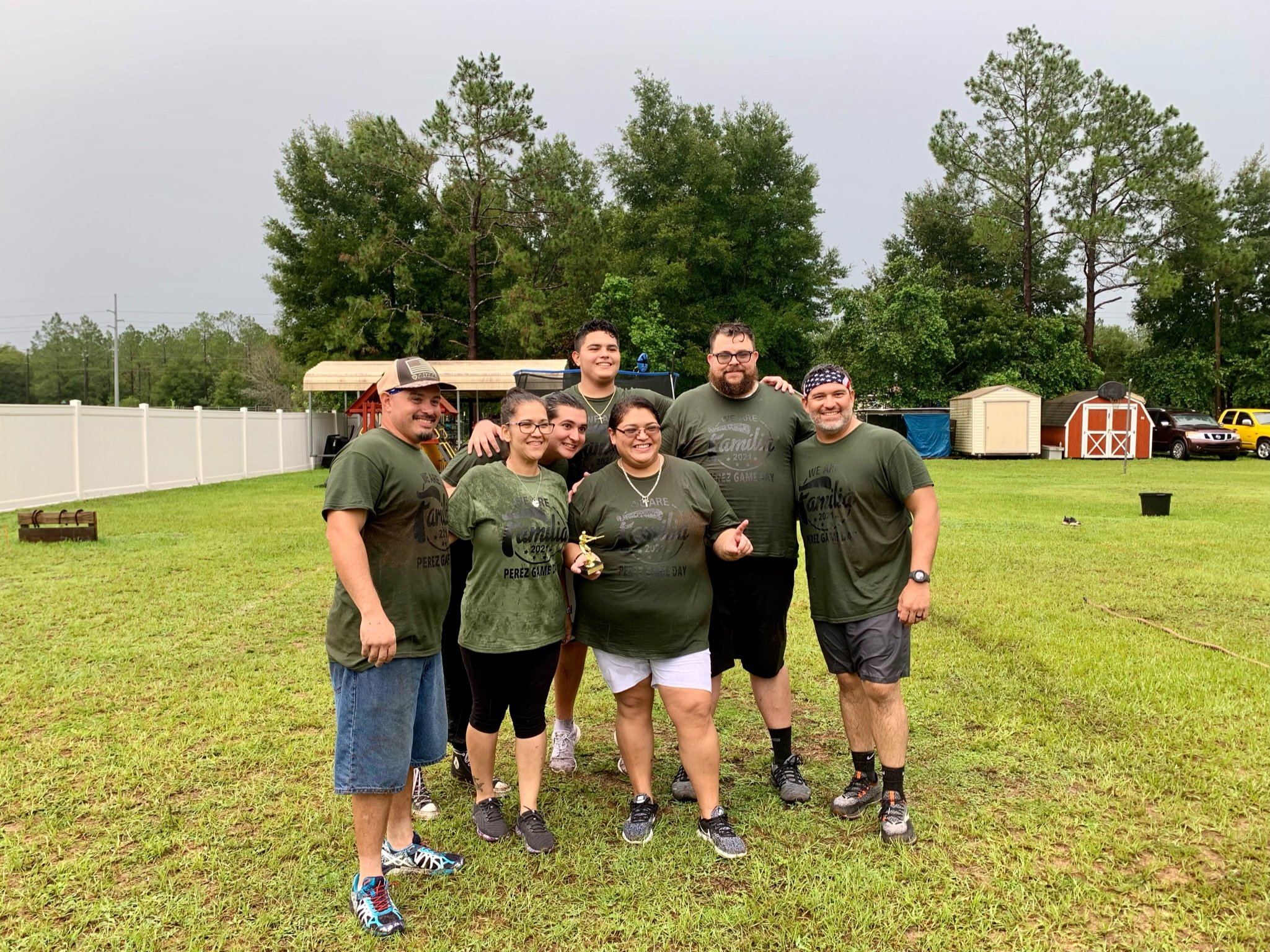 Group of people wearing matching green shirts posing outdoors on grass.