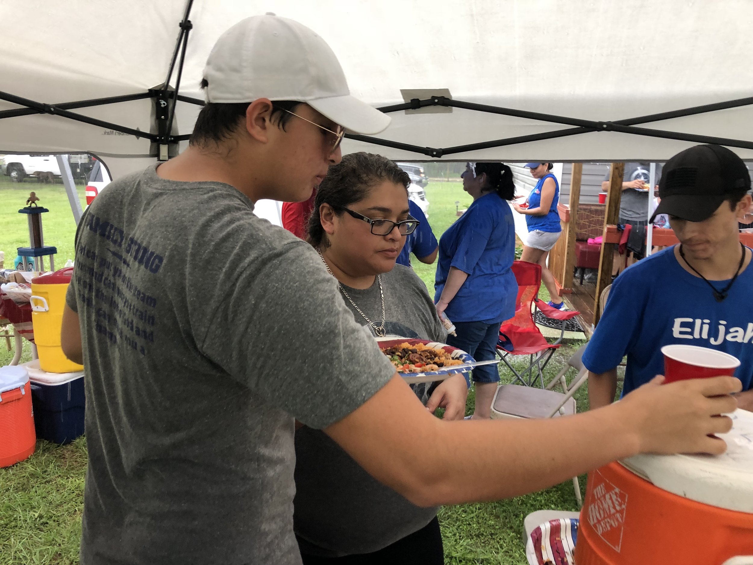 People gathered under a tent at an outdoor event, holding food and drinks.