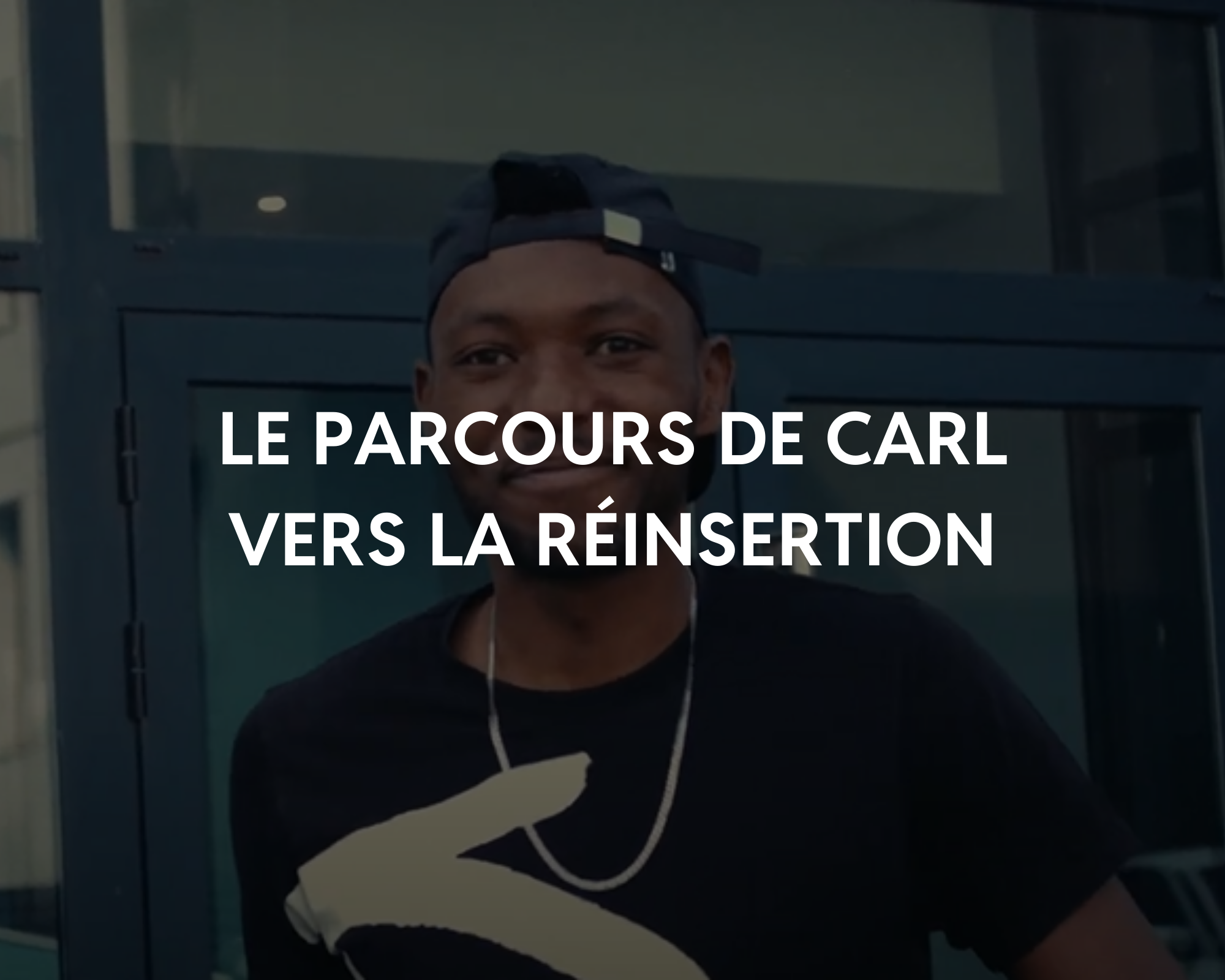 Jeune homme portant une casquette et un t-shirt noir, souriant, devant une porte en verre