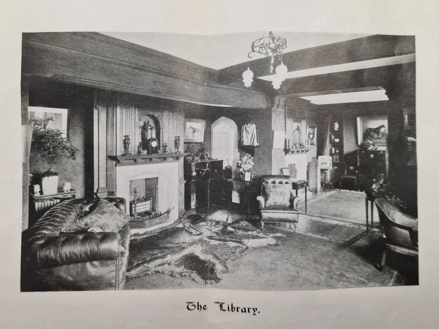 Historic photograph of the Library at Lanwades Hall, showing wood-panelled walls, fireplace, and period furnishings.