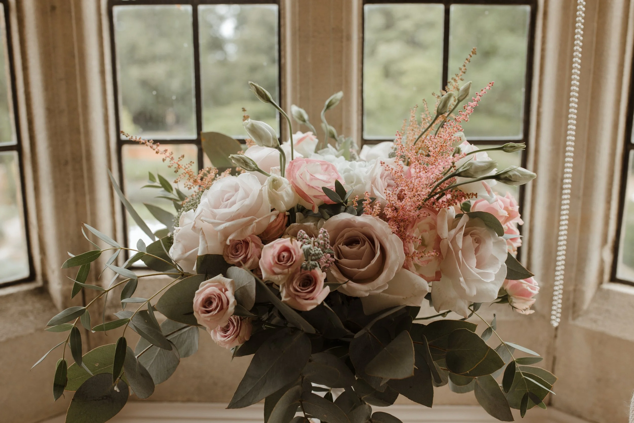 Elegant floral arrangement in soft pink and ivory tones at Lanwades Hall, Suffolk, displayed in a bay window for a private event