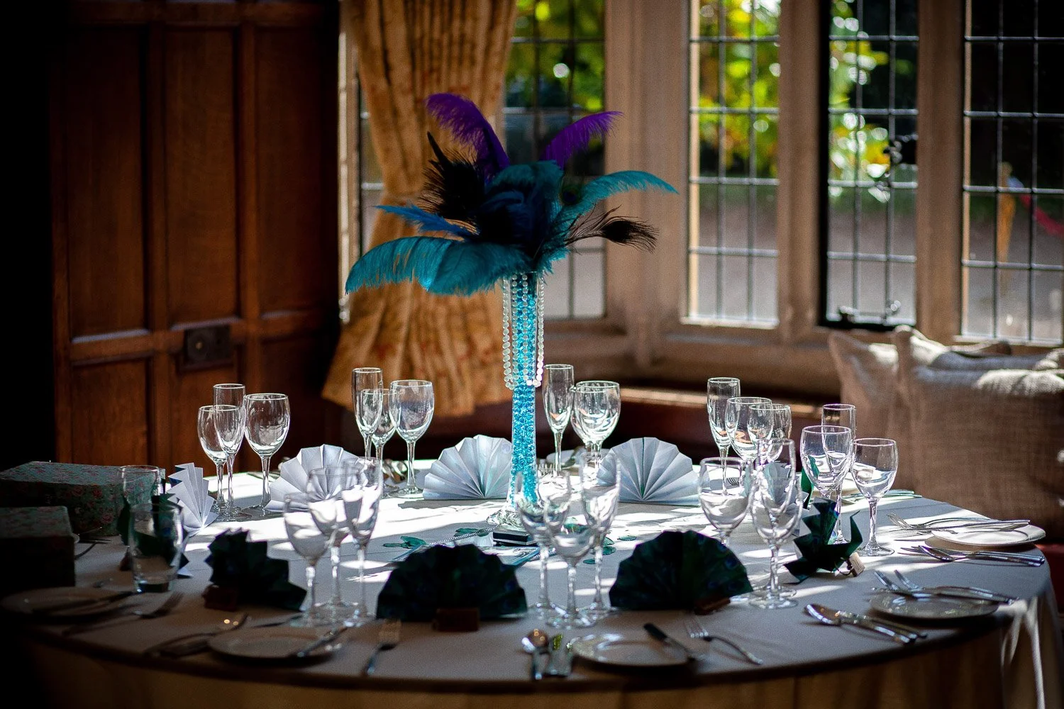 Elegant dinner table setup at Lanwades Hall, Suffolk, with crystal glassware and a vibrant feather centrepiece for a private celebration