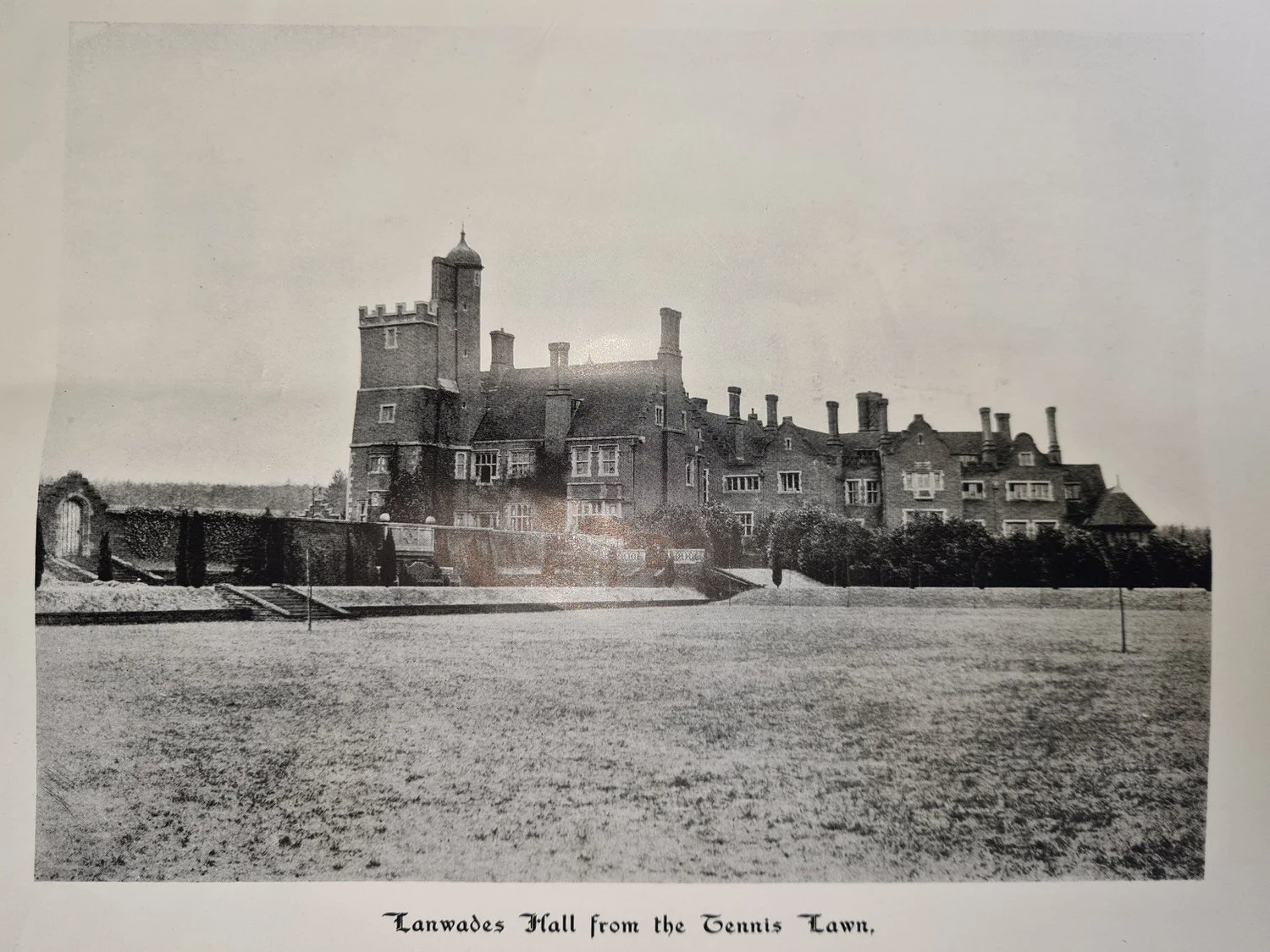 Historic photograph of Lanwades Hall viewed from the tennis lawn, showing the full façade and landscaped grounds.