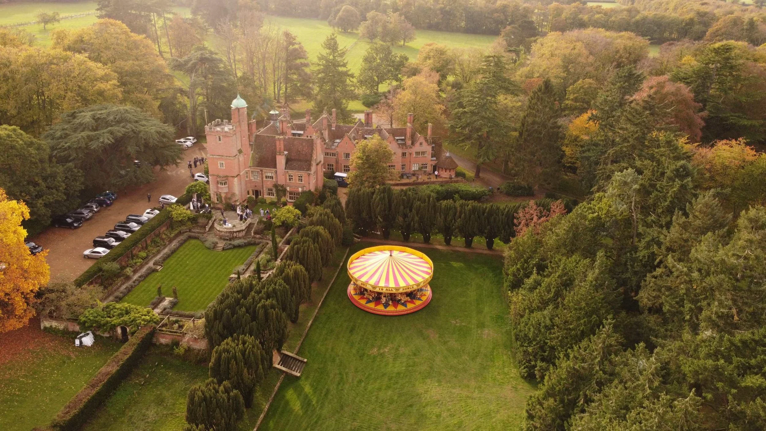 Aerial view of Lanwades Hall, Suffolk, showing beautiful gardens and a traditional carousel set up for a summer party event