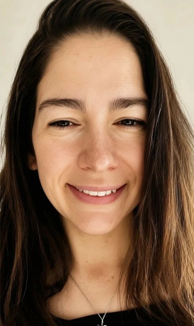 Close-up of a young woman with long brown hair, smiling with slightly closed eyes, wearing a black top and a silver necklace.