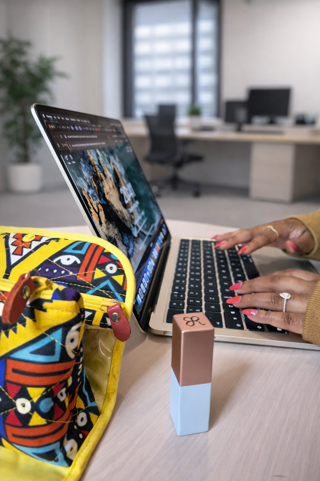 Person working on a laptop with colorful backpack, lipstick, and ring on hand in an office.