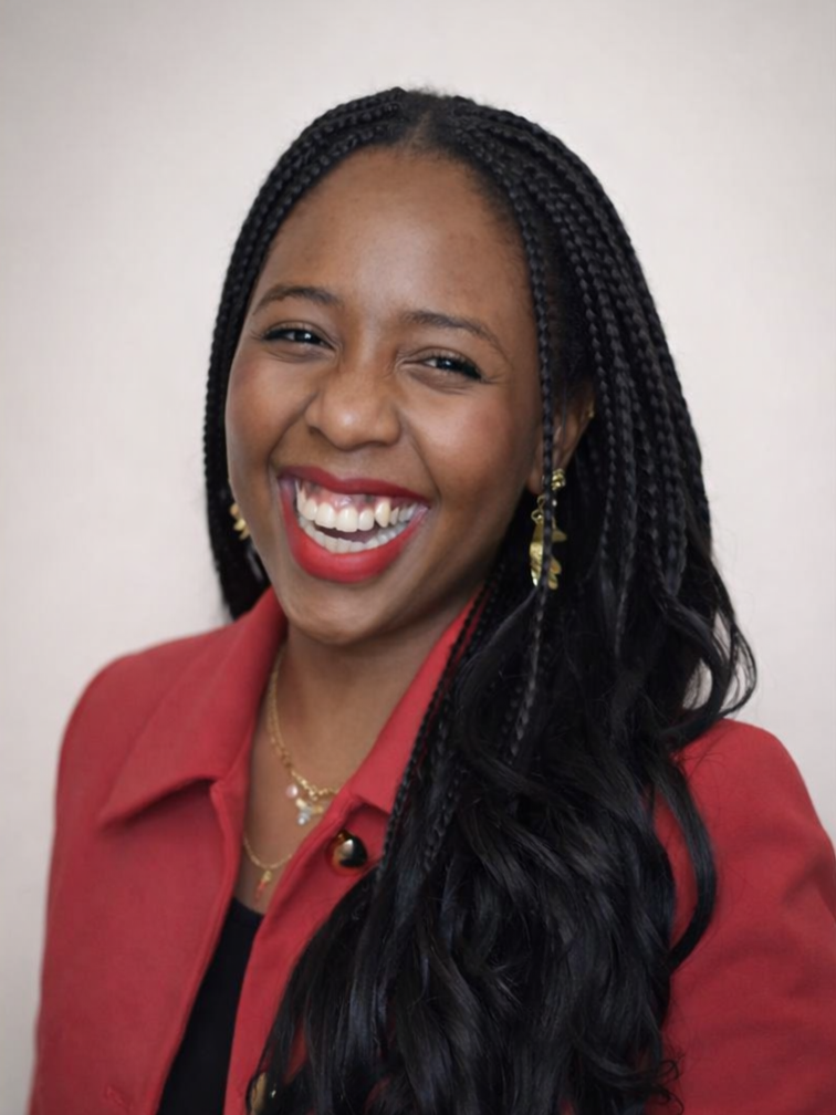 A smiling woman with dark braided hair, wearing a red jacket, gold earrings, and a gold necklace.