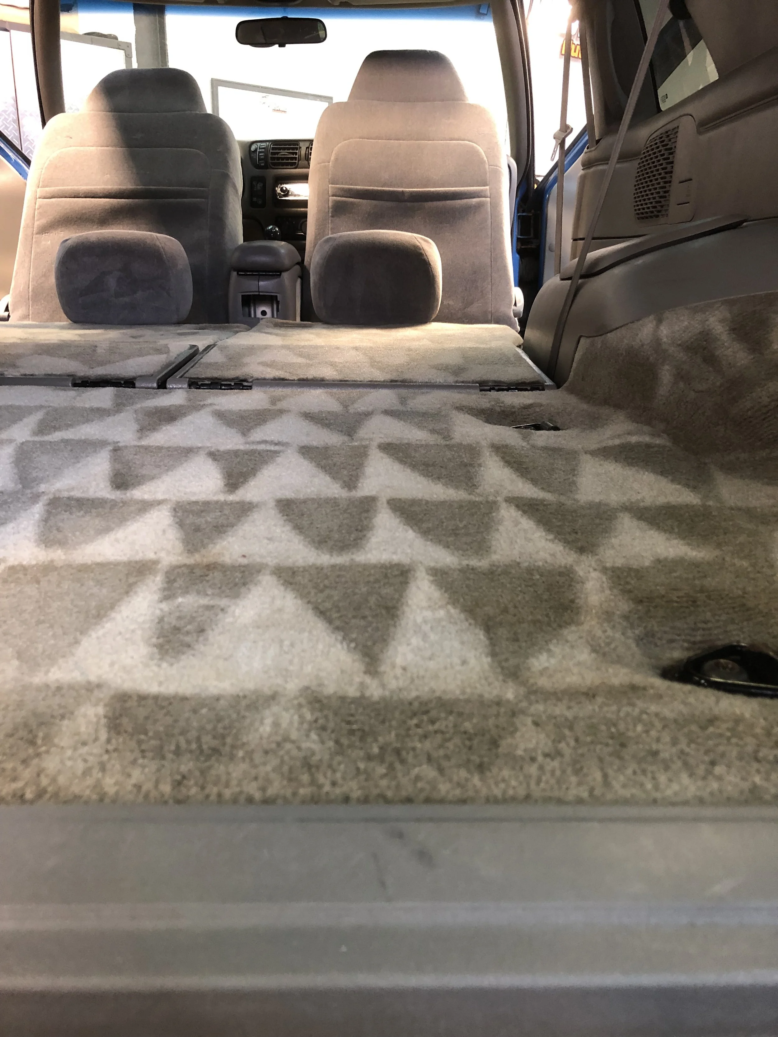 Interior of a vehicle showing the rear cargo area with a patterned carpet, and the backs of the second-row seats.