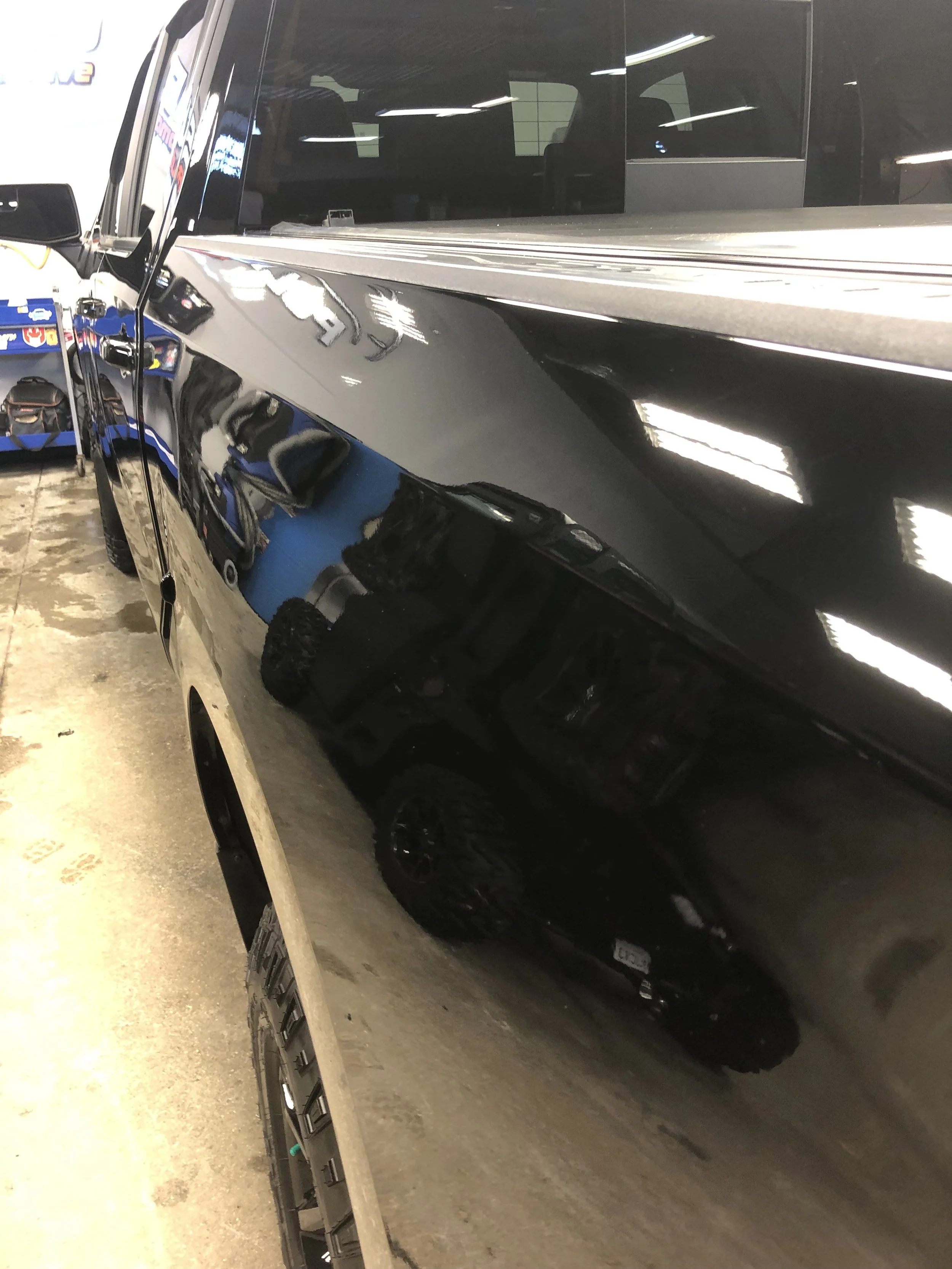 Close-up of a black vehicle's shiny exterior, showing reflections of the garage and equipment.