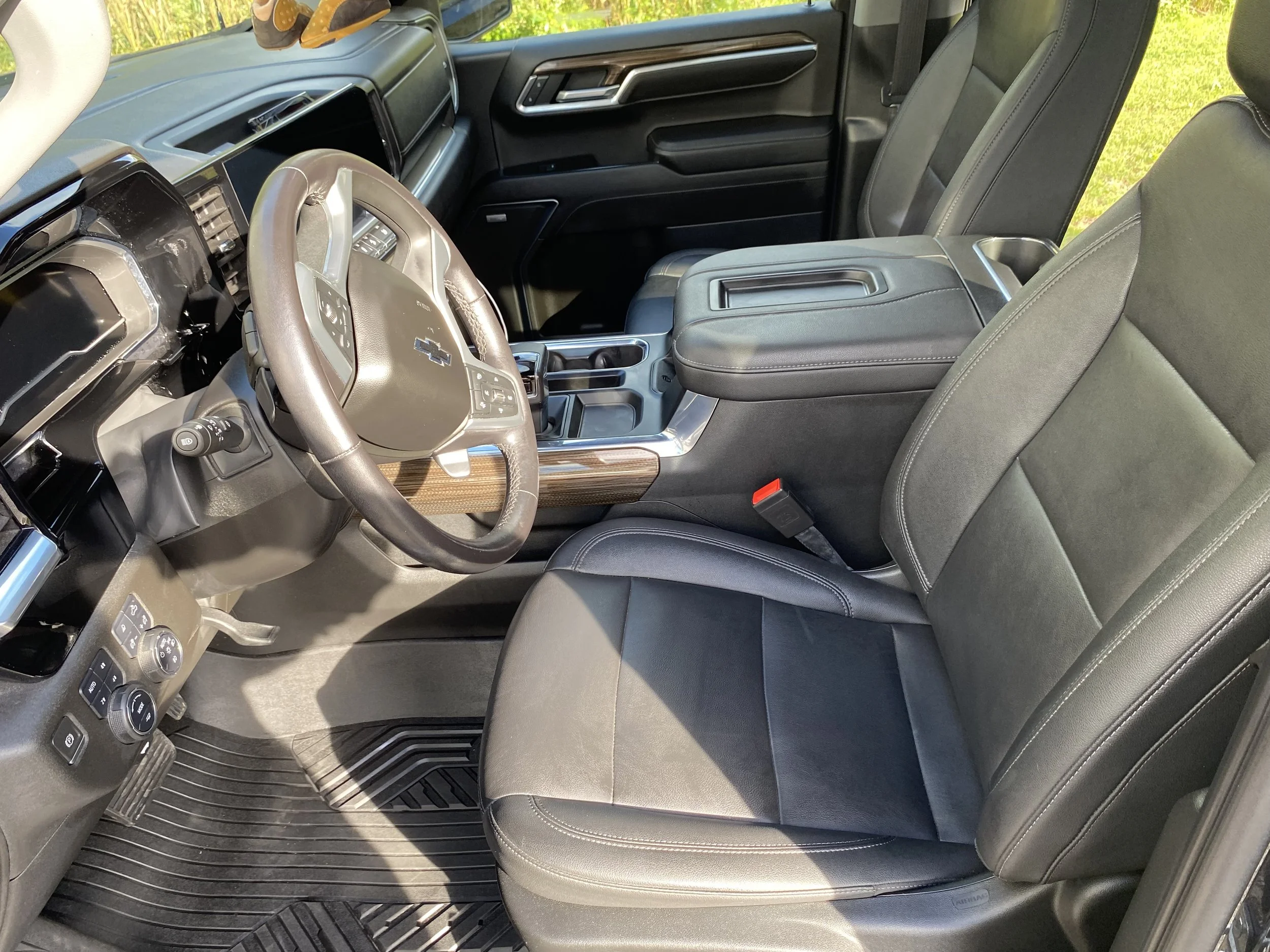Interior of a modern vehicle, showing the driver's seat, steering wheel, dashboard, and center console with a closed lid and cup holder, all in black with some wood trim accents.
