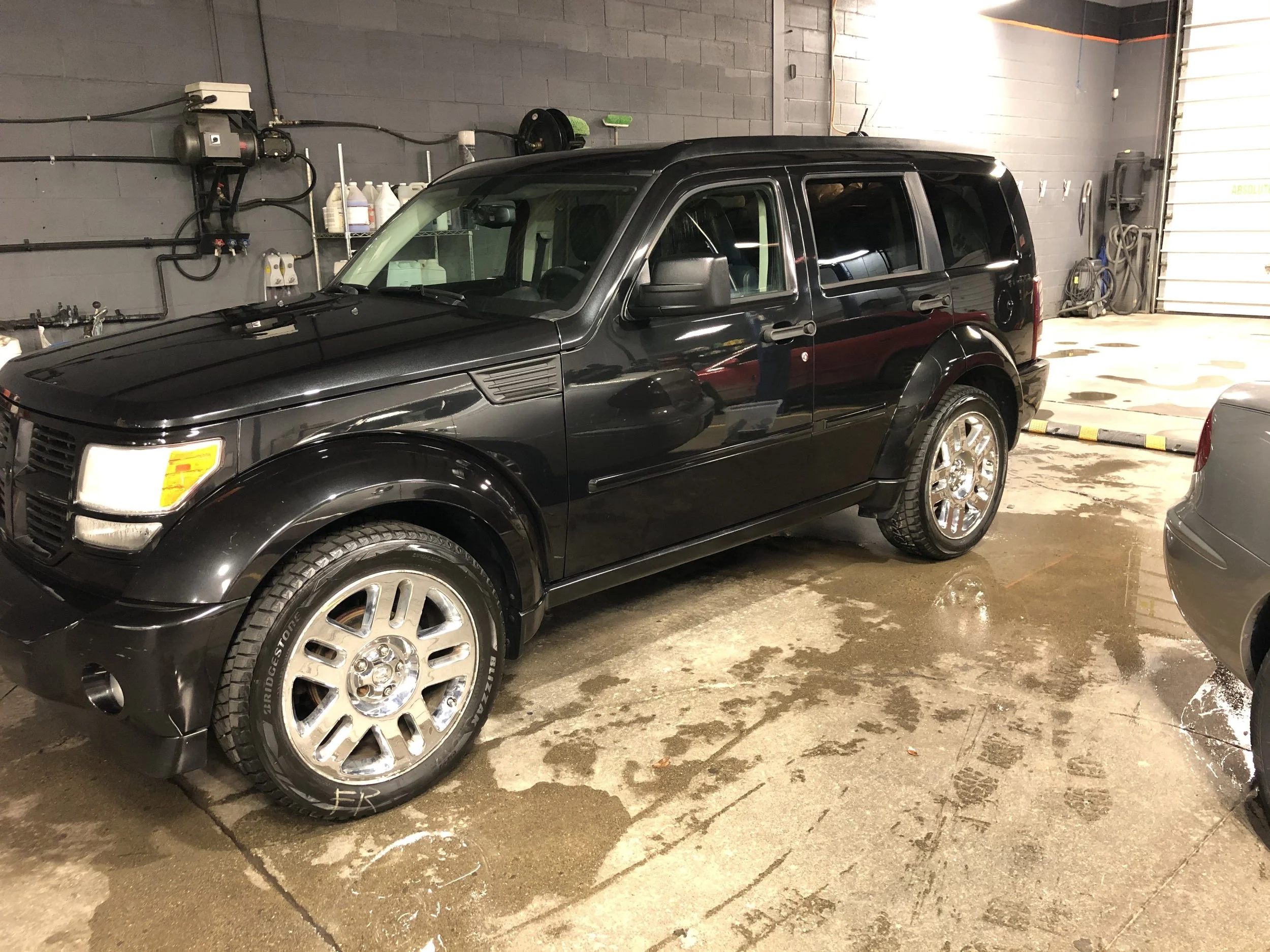 Black SUV parked inside a clean garage with a concrete floor, reflected water patches, and garage tools and equipment in the background.