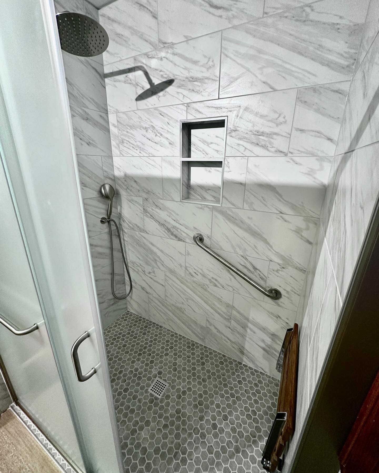 Grey shower for a wonderful clients. Older couple asked for a bench that &ldquo;could easily go away if need be&rdquo; say no more! We like the small teak bench that folds up for non needed purposes or folds down when needed! Curb-less entry shower a