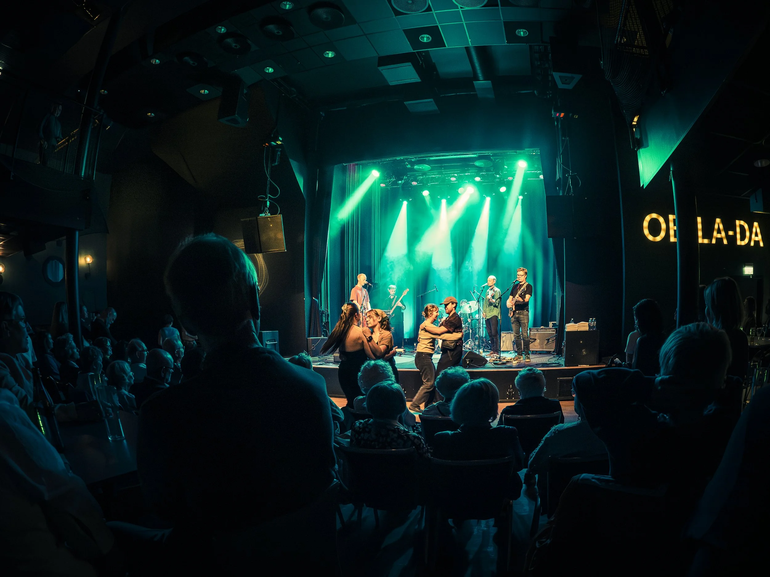 Konsertlokale med musikarar på scena og publikum som dansar