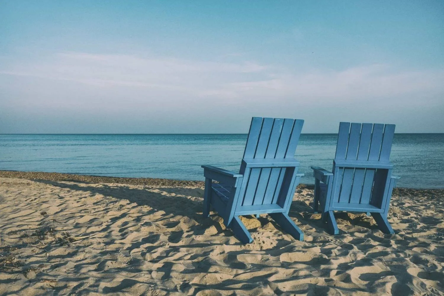 Beach scene with two blue lounge chairs facing the water