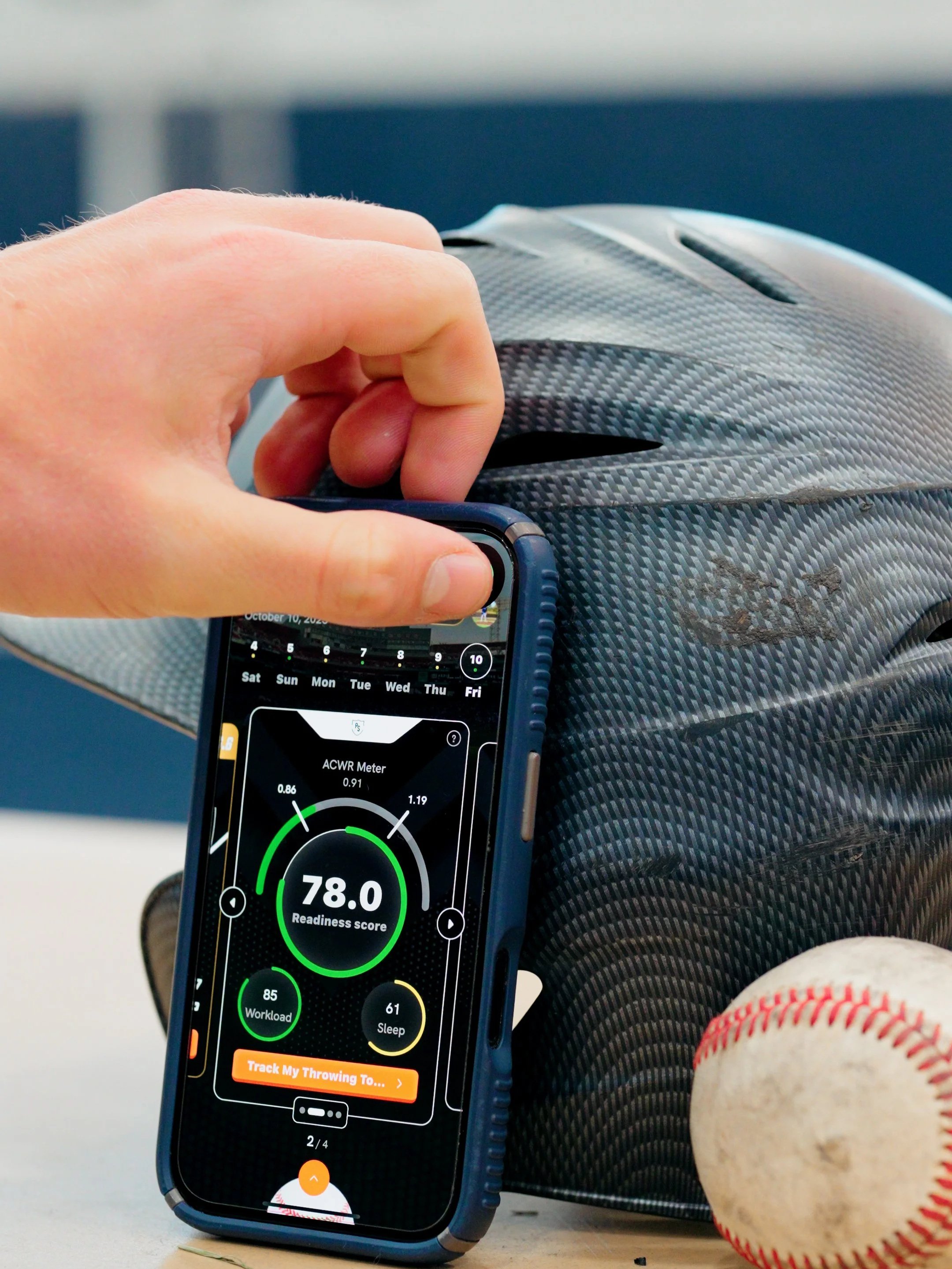 Close-up of a person's hand holding a phone displaying a readiness score app, resting on a baseball glove with a baseball beside it.