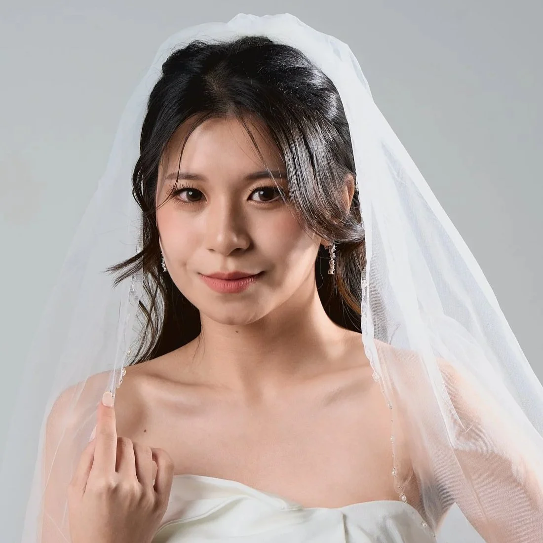 A woman in a wedding dress and veil, looking at the camera with a slight smile.