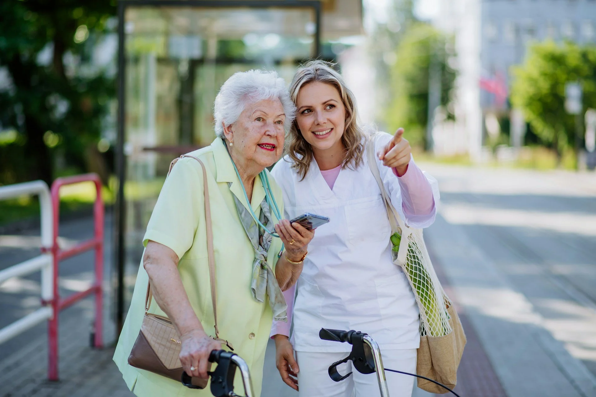 A caregiver helps an older woman navigate in public with the help of a cellphone